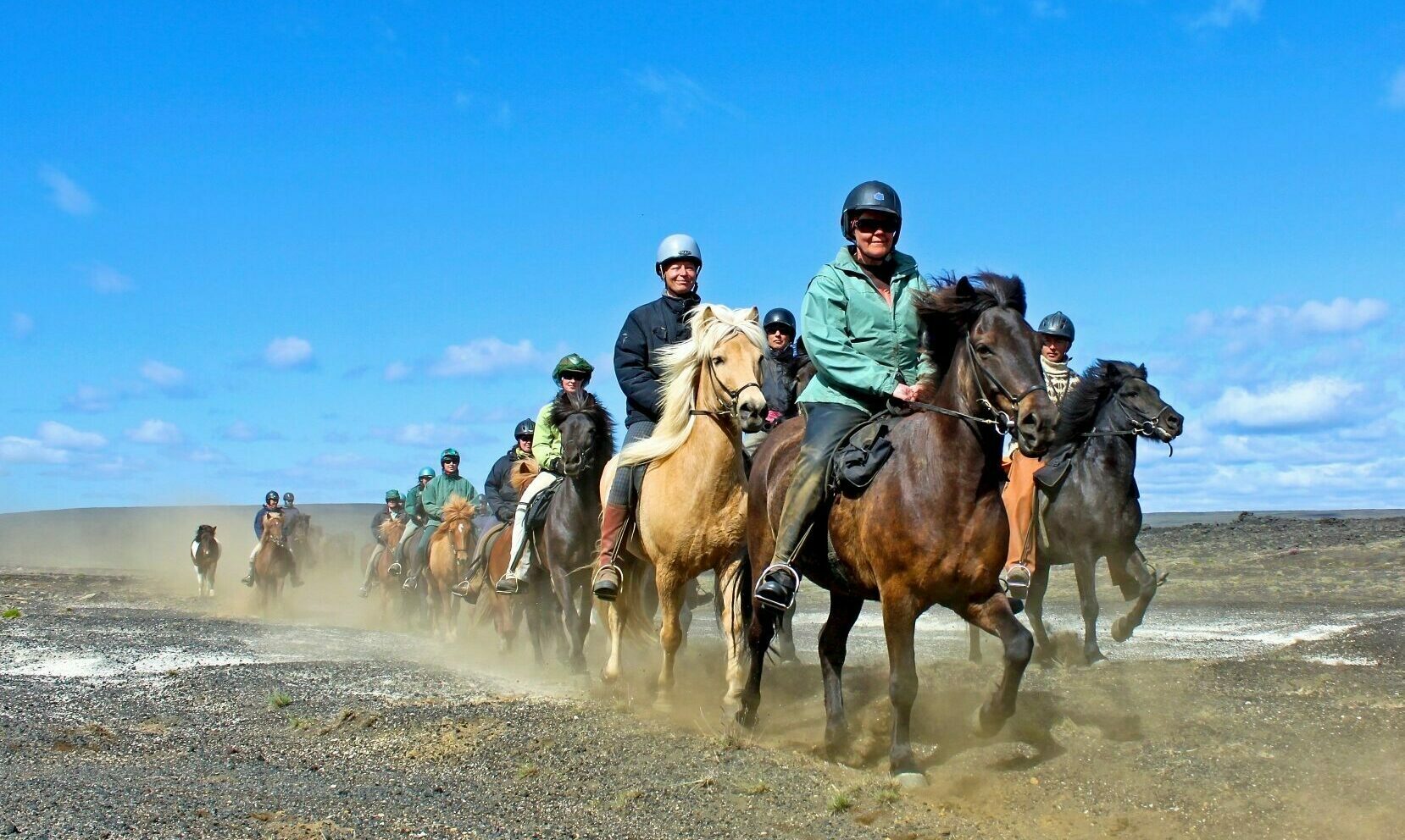 Reittour Islandpferde Islandreise;
Gruppe reitet in sortiert in Zweier-Reihe über karge Landschaft und wirbelt dabei Staub auf.