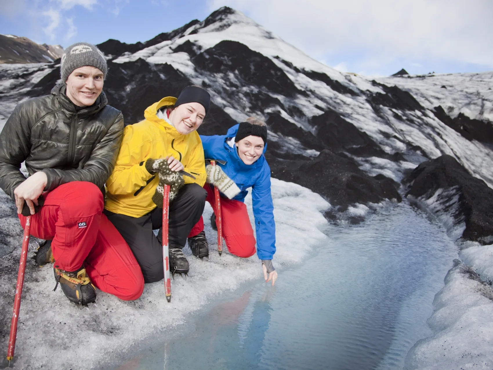 Drei Personen neben einer kleinen Gletscherquelle bei einer Gletscherwanderung am Solheimajökull
