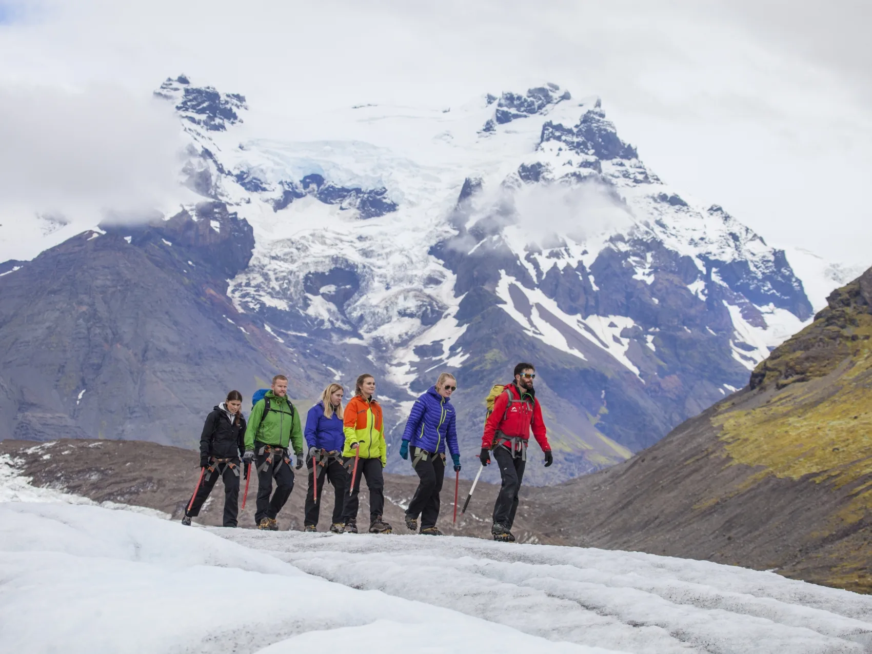 Fünf Personen zusammen mit einem Guide bei einer Gletscherwanderung mit einem verschneiten Berg im Hintergrund