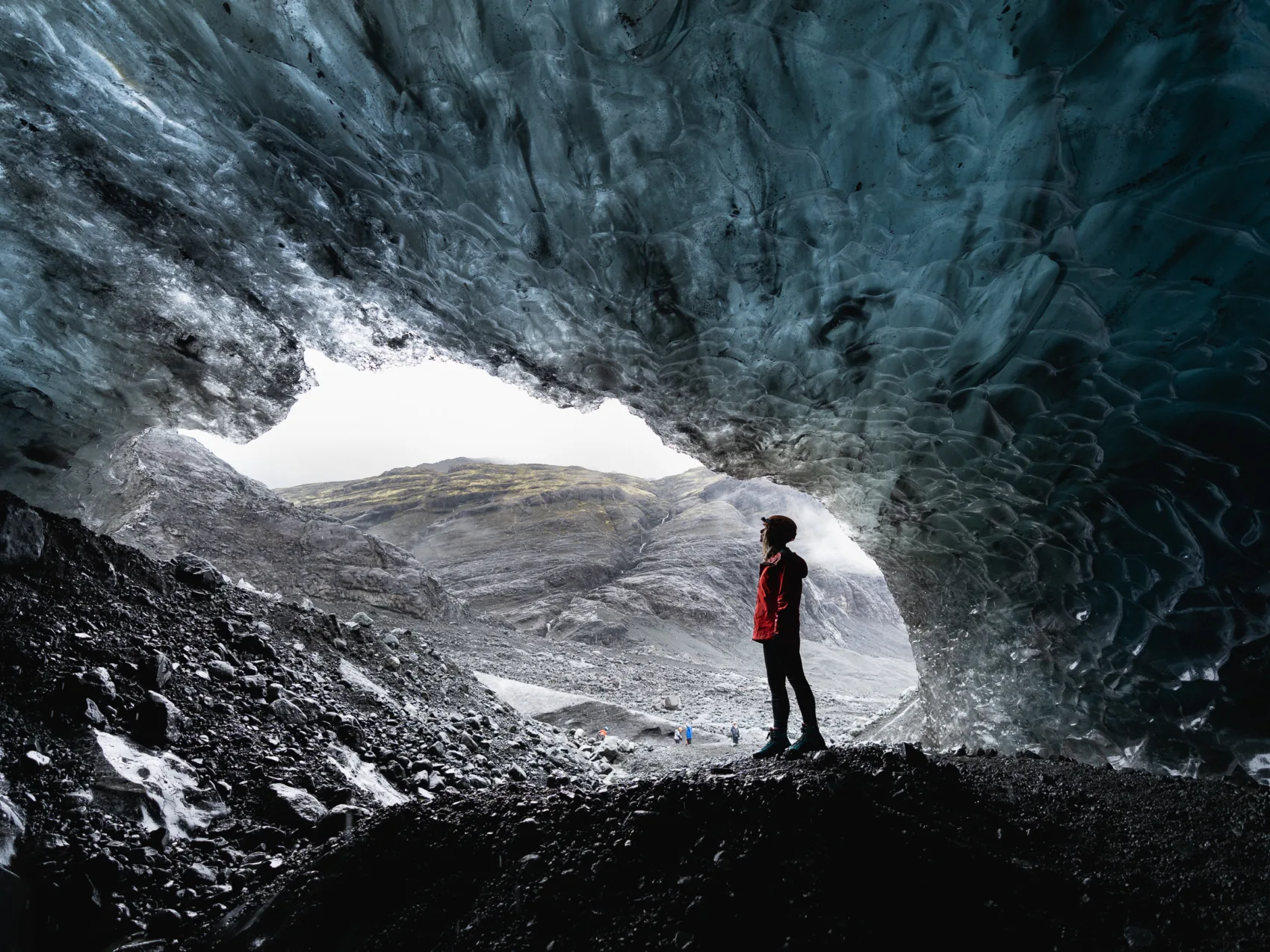 Frau, die am Ausgang einer Eishöhle in Island steht mit einem Berg im Hintergrund