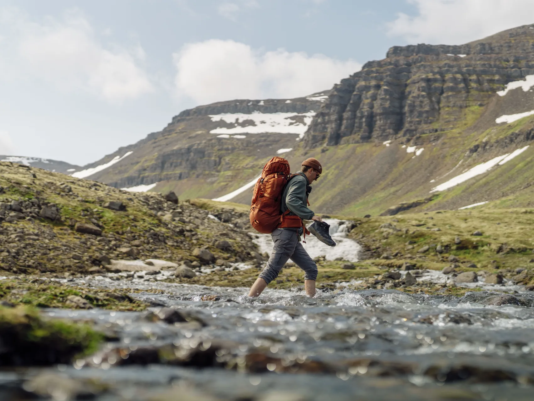 Wandernder Mann im Gebiet Hornstrandir in den Westffjorden Islands der Barfuß durch einen Fluss geht um auf die andere Seite zu kommen