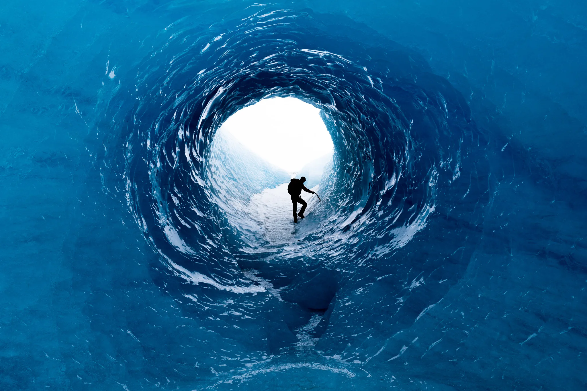 Mann, der durch eine runde blaue Eishöhle in Island läuft