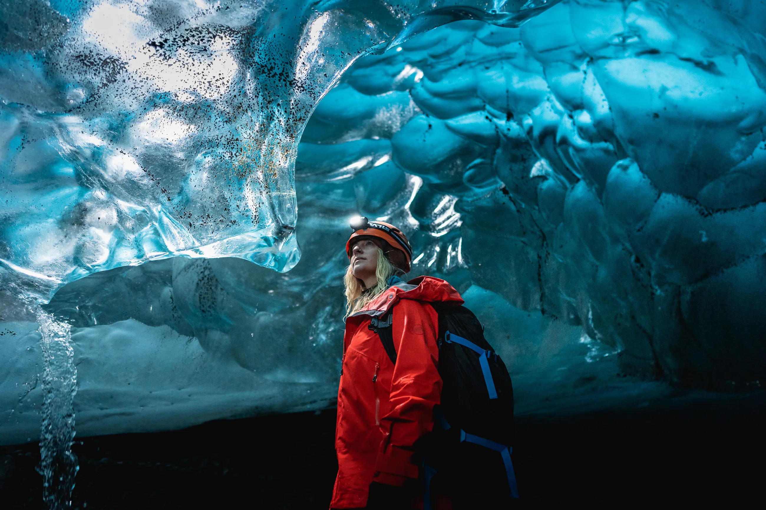 Frau, die im inneren einer schönen blauen Eishöhle in Island steht und sie bewundert