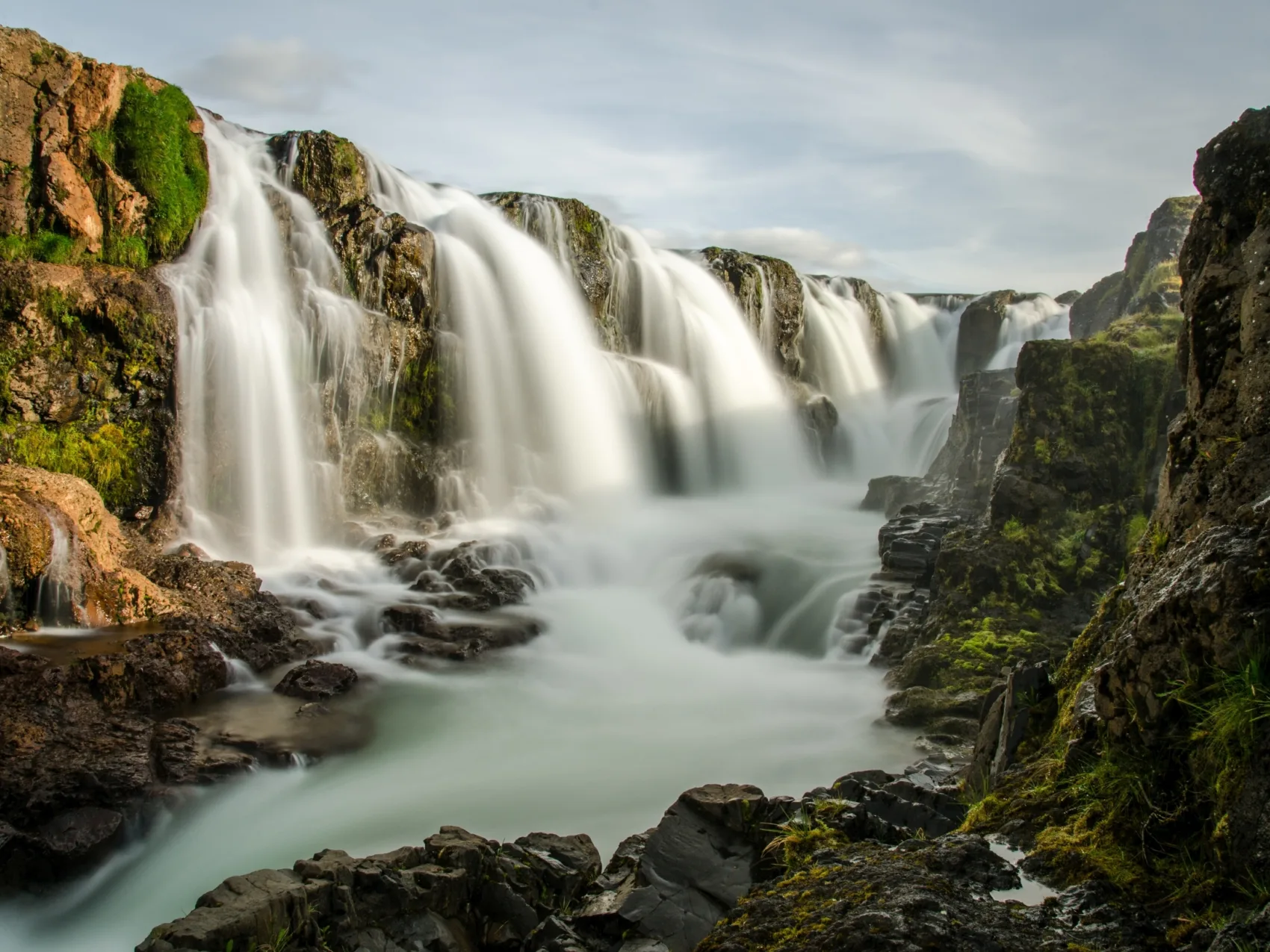 Mitreißende Wasser, Foto: Katharina Klein
Viele einzelne Wasserfälle nebeneinander in einer steinigen Schlucht mit teils grün bewachsenen Hängen