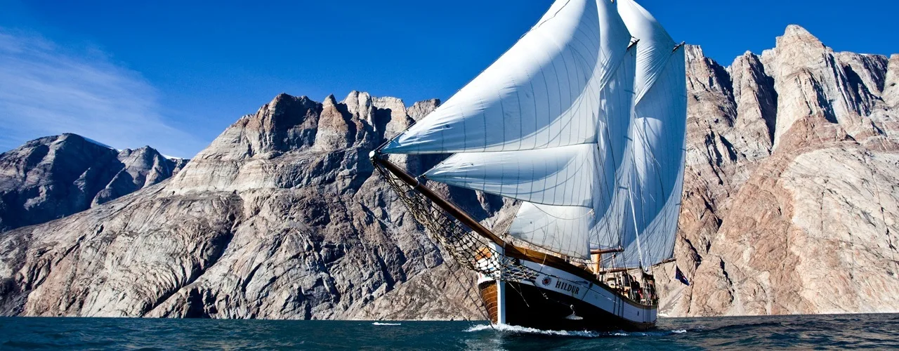 Segelschiff Hildur, Grönland vor einem schroffen, steinigen Gebirge .