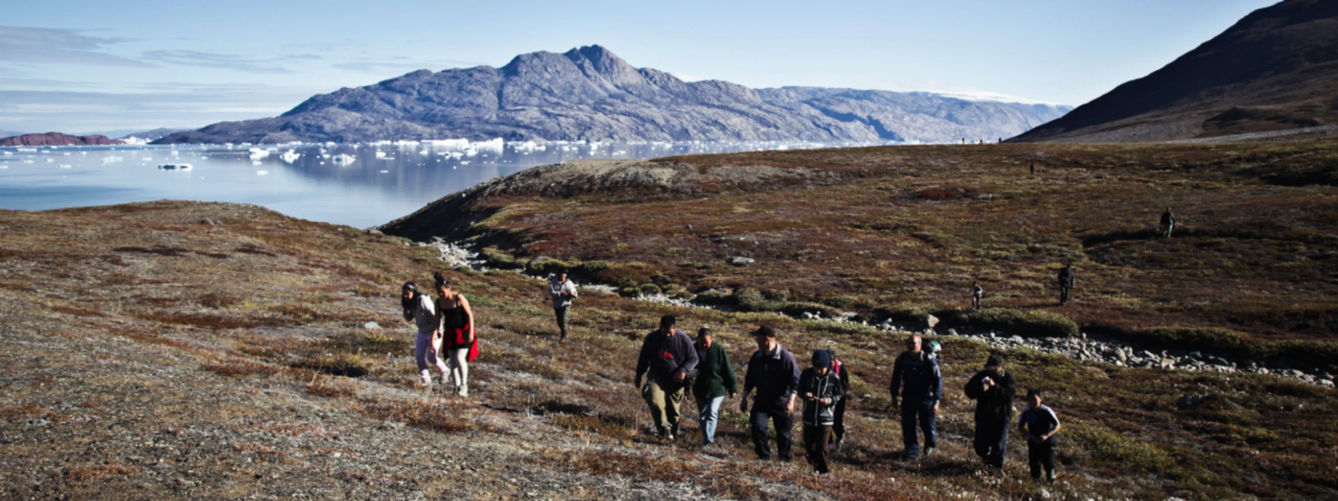 Wanderung in Scoresbysund, Ostgrönland
Wandergruppe geht Hügel bergauf
karge Landschaft, im Hintergrund Eisfjord