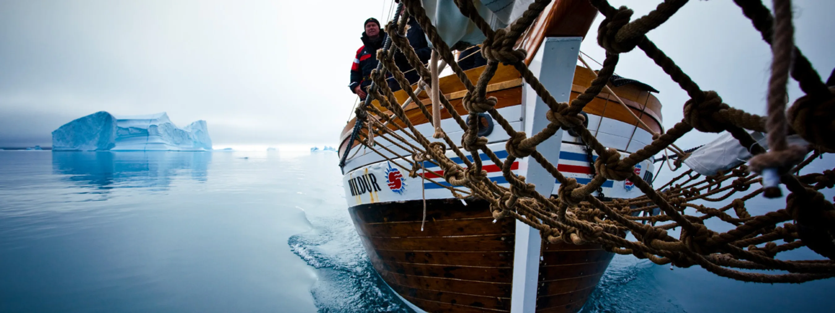 Segelschiff von vorne unten abgebildet. Im Hintergrund Eisberge