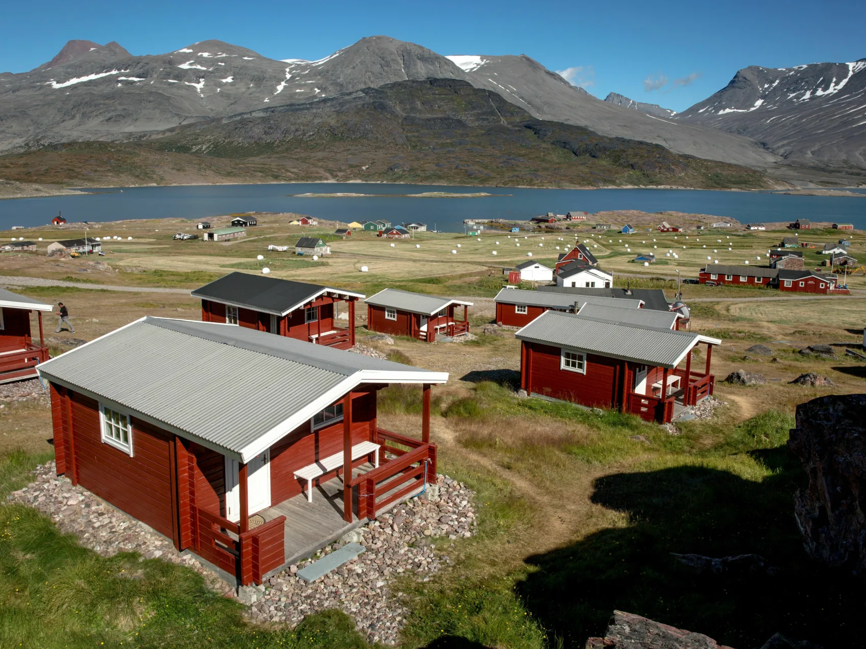Einzelne rote Hütten mit Bergen und Fjord im Hintergrund