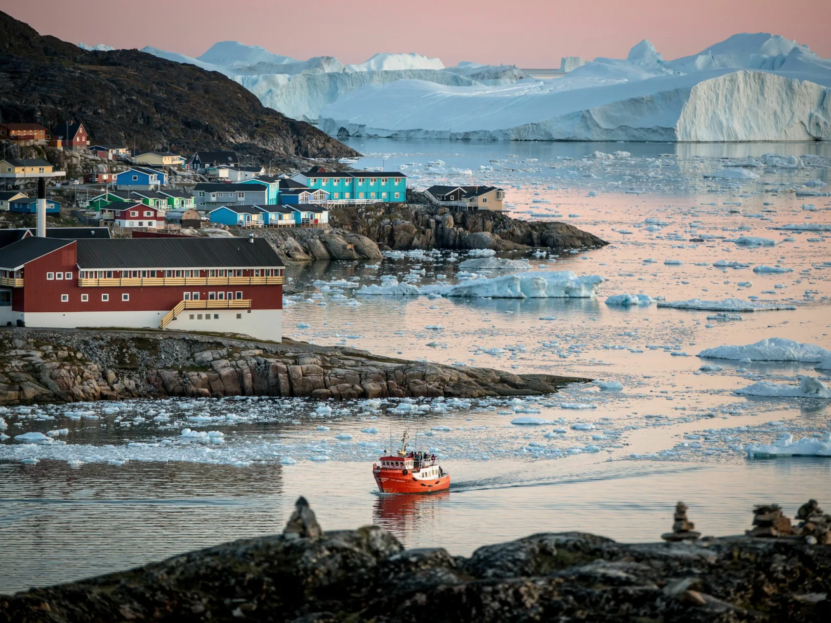 kleines Schiff fährt im Hafen ein, im Hintergrund Eisberge und kleine Stadt