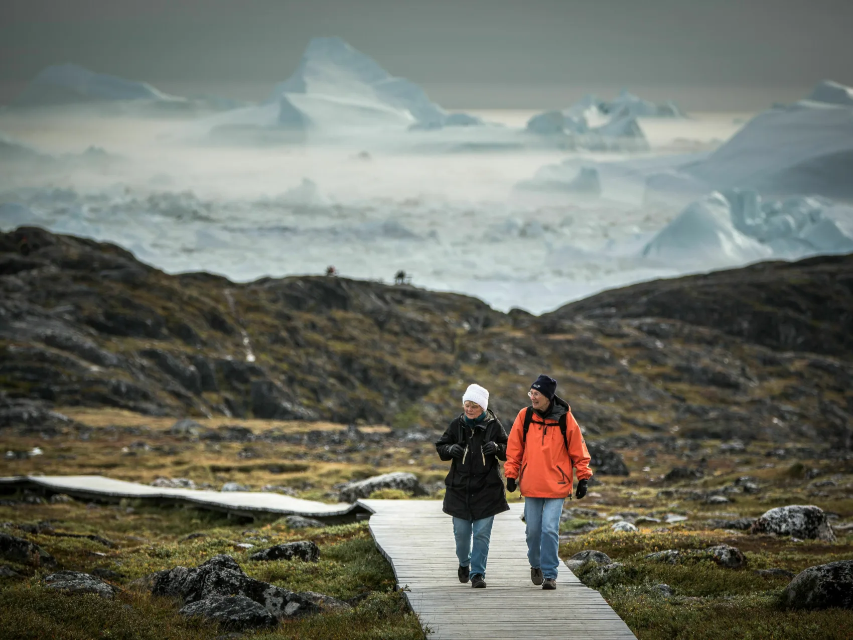 Ein Ehepaar spaziert bei Sermermiut, im Hintergrund befinden sich Eisberge
