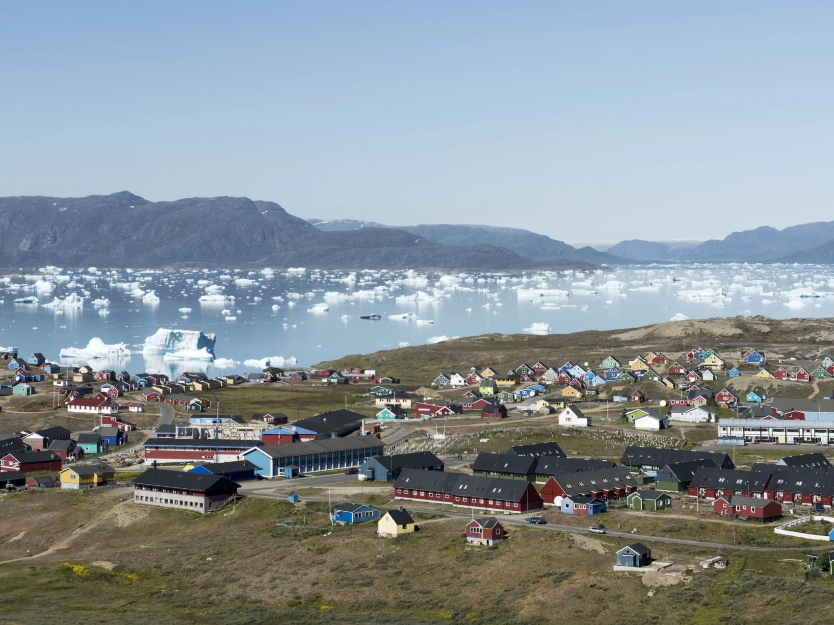 Siedlung mit vielen Häusern in verschiedenen Farben und Fjord mit vielen kleinen Eisbergen im Hintergrund