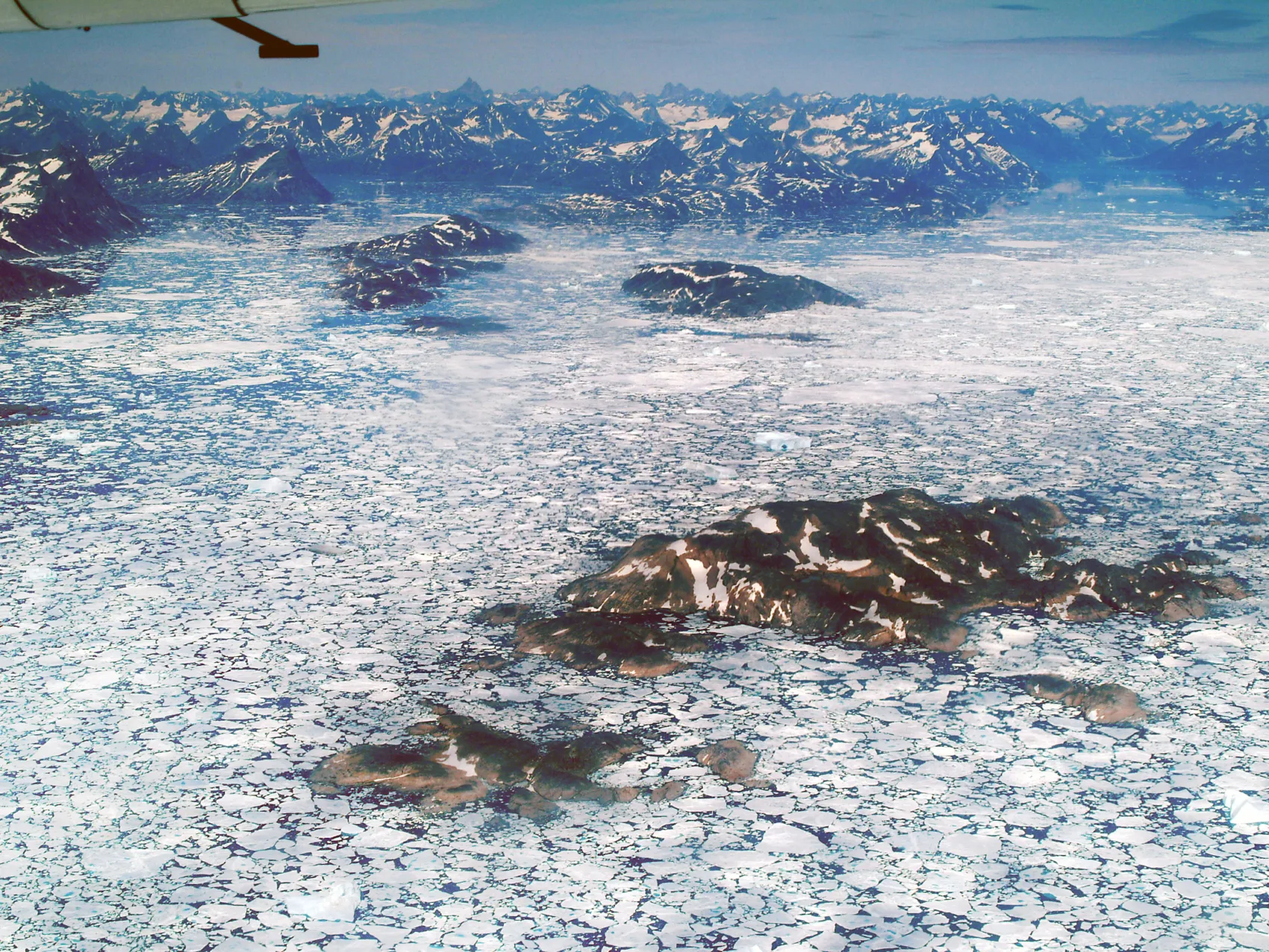 Luftaufnahme von Eisbergen in Ostgrönland, schroffes Gebirge und hohe Berge im Hintergrund