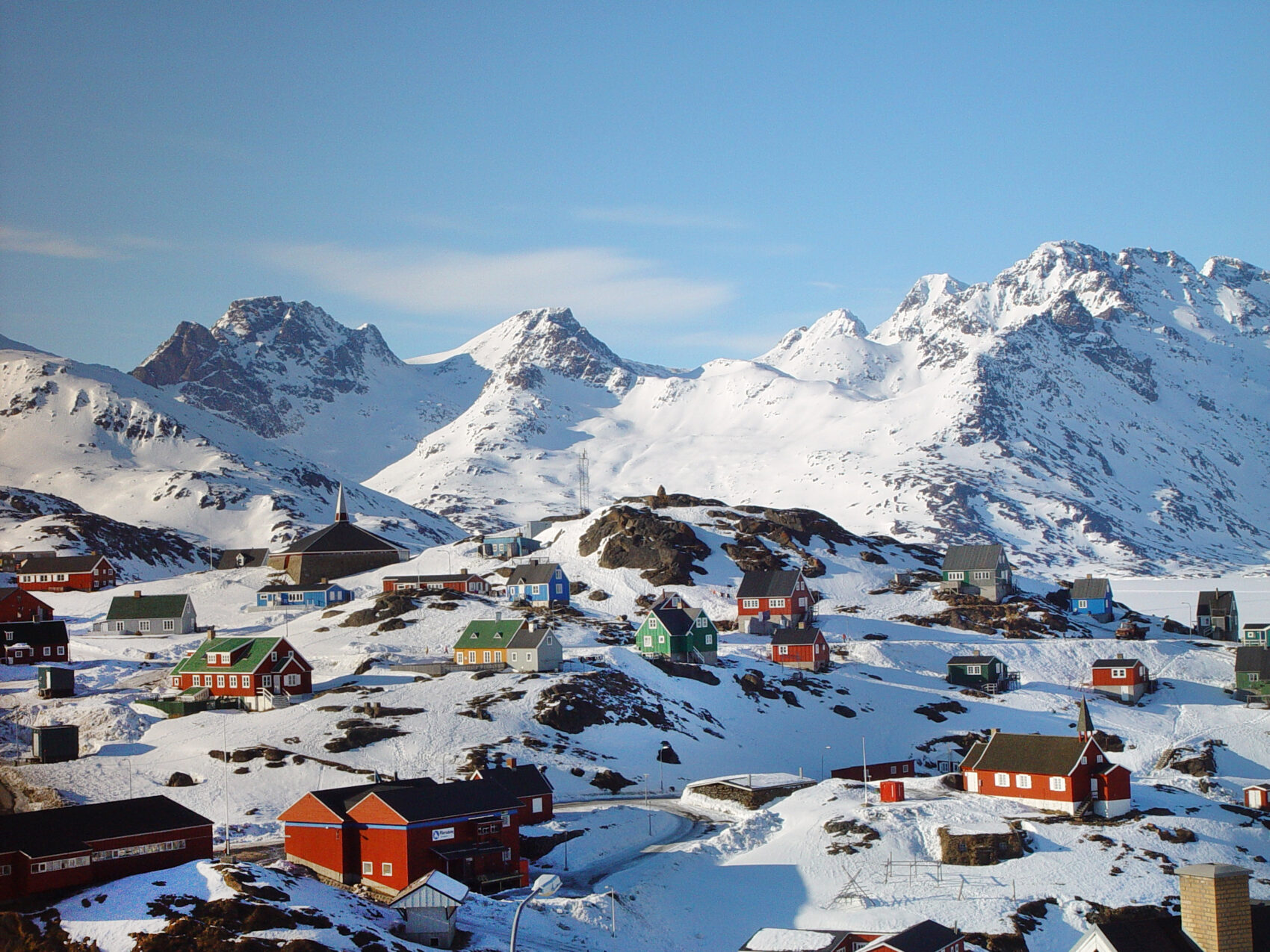 Ostgrönland Siedlung mit Schnee, Häuser liegen verteilt auf felsigen gebiet im Schnee, im Hintergrund Berge ebenfalls beschneit