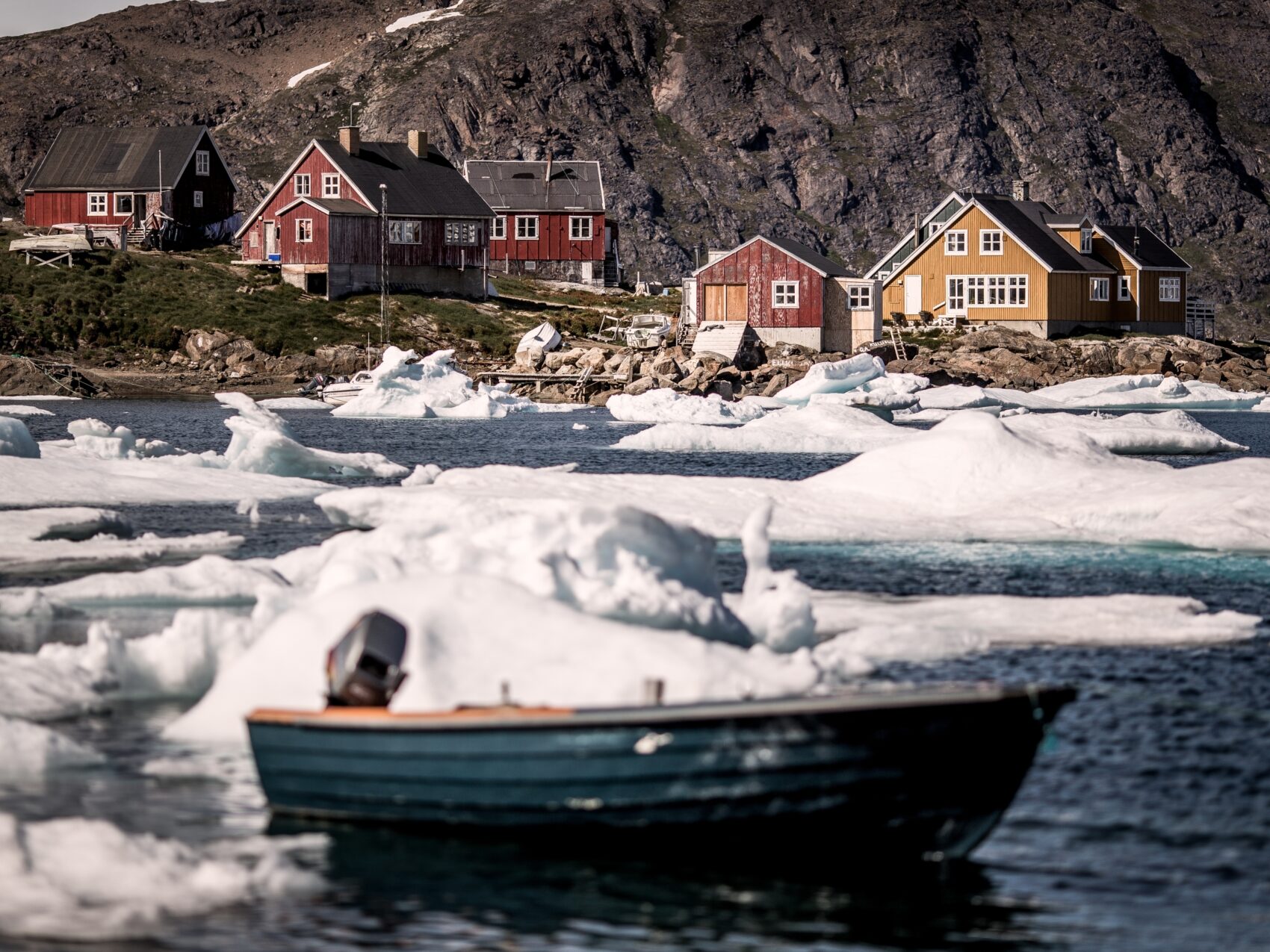 Ostgrönland Kulusuk Häuser liegen an einer Bucht, kleines Boot und Eisberge auf dem Wasser.