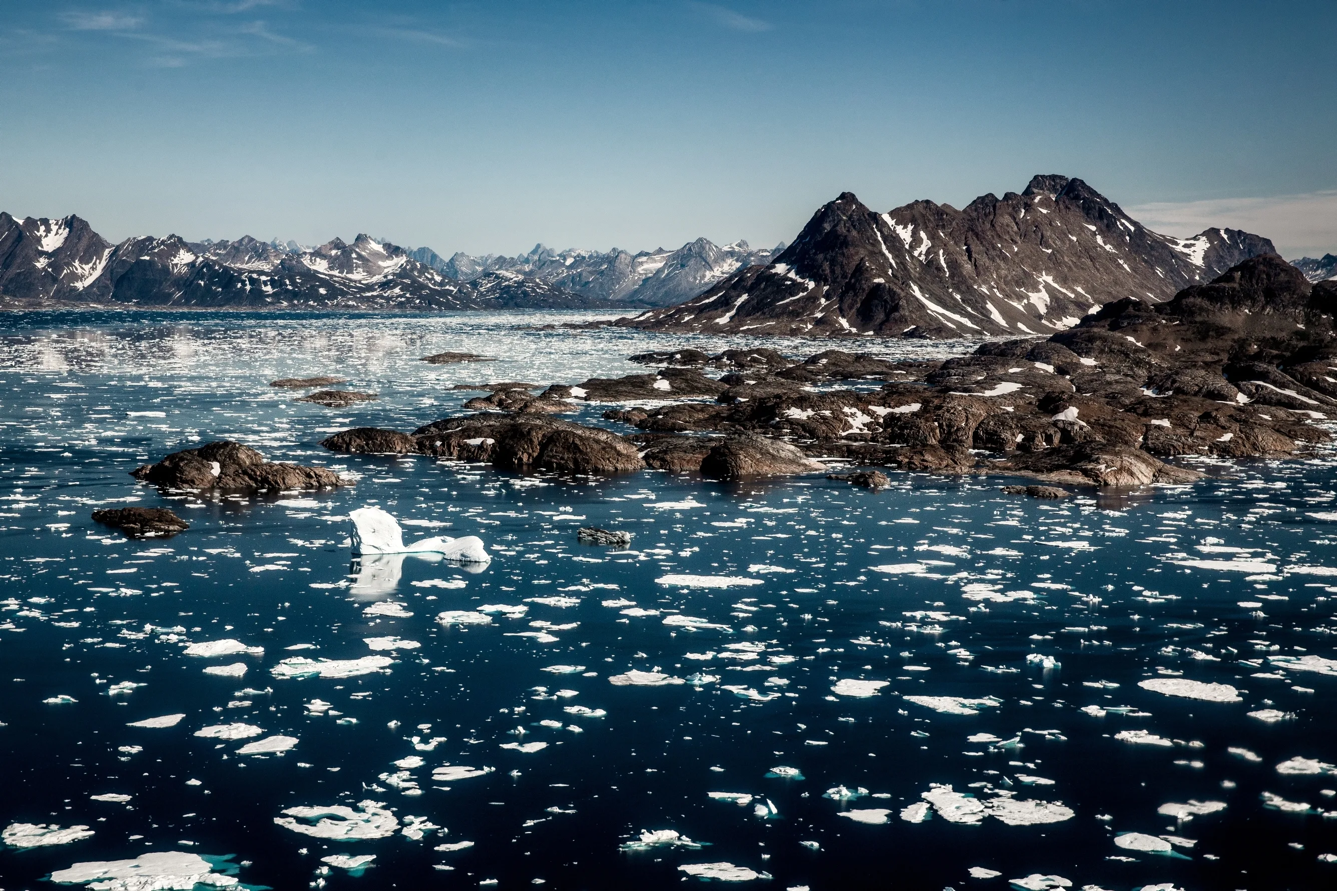 Eisschollen schwimmen im Fjord, umgeben von schroffen Gestein und Gebirge.