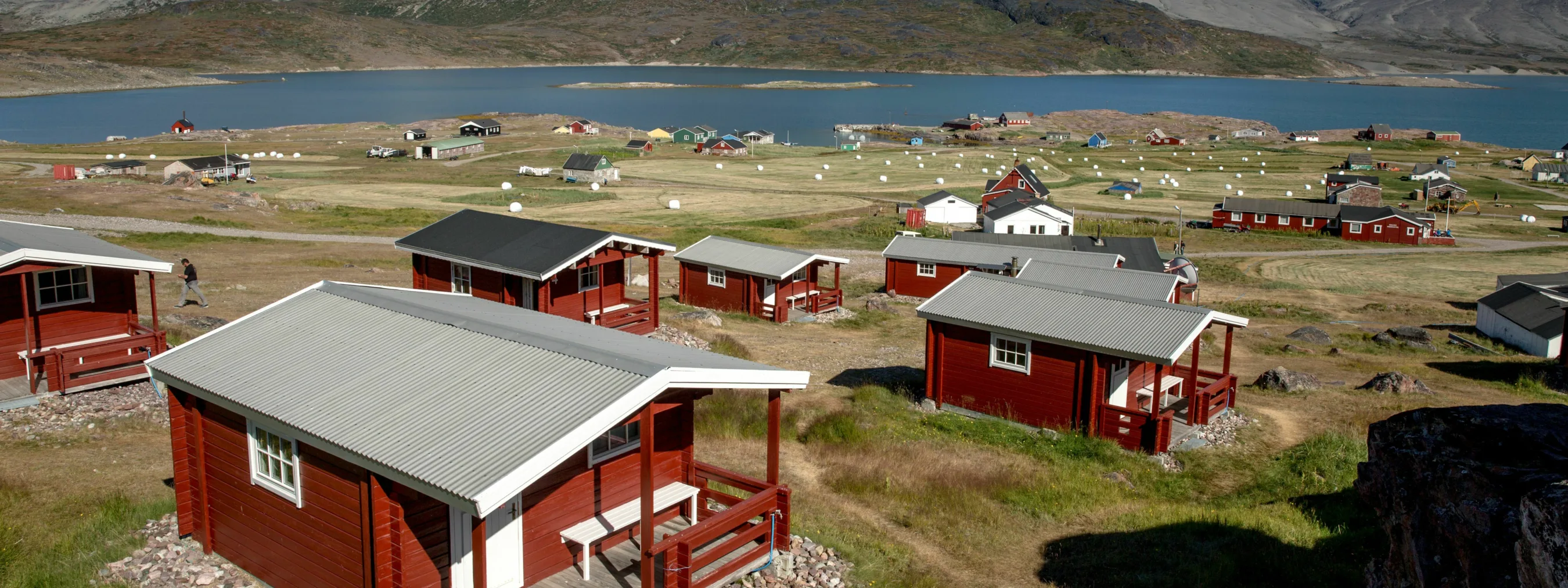 Einzelne rote Hütten mit Bergen und Fjord im Hintergrund