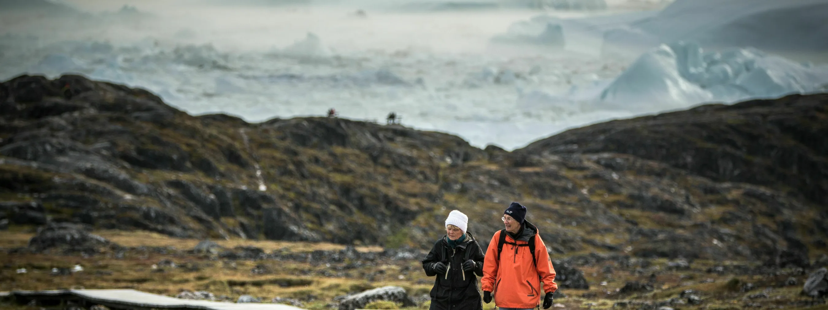 Ein Ehepaar spaziert bei Sermermiut, im Hintergrund befinden sich Eisberge