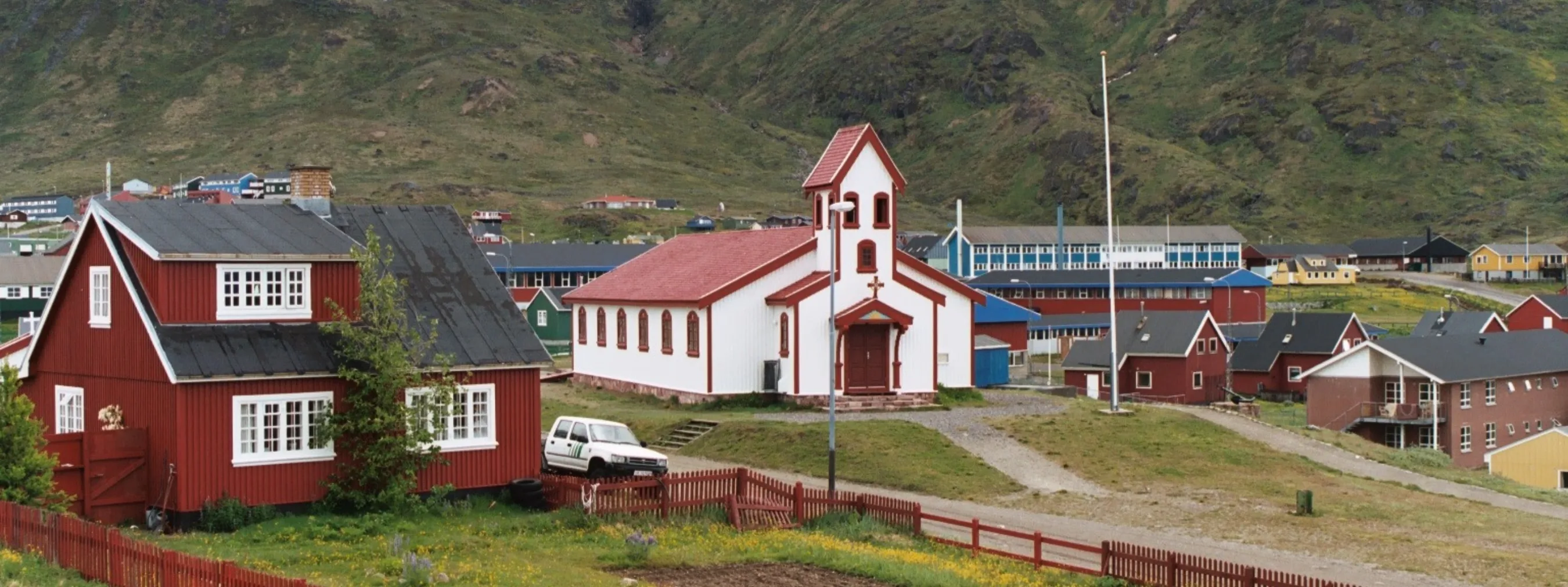 Siedlung Narsaq in Südgrönland, Häuser und Kirche vor Bergen mit Nebel