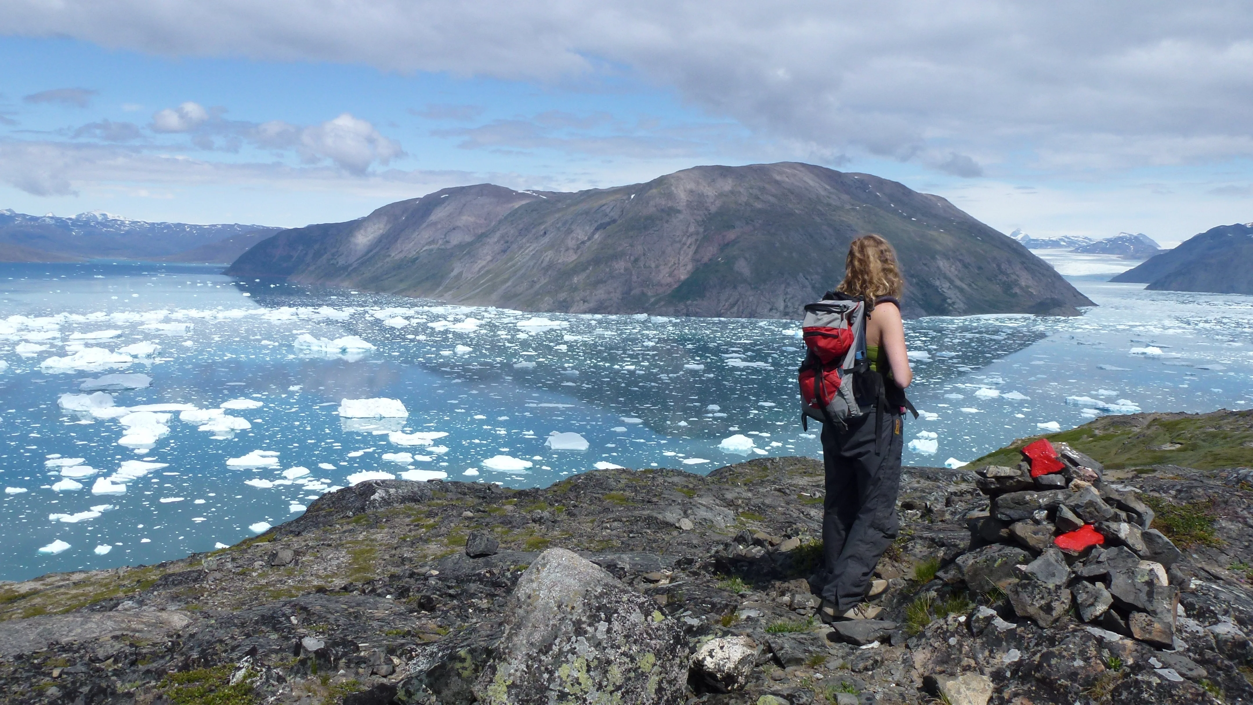 Eine Wanderin blickt auf einen Eisfjord mit mehreren schönen Bergen im Hintergrund