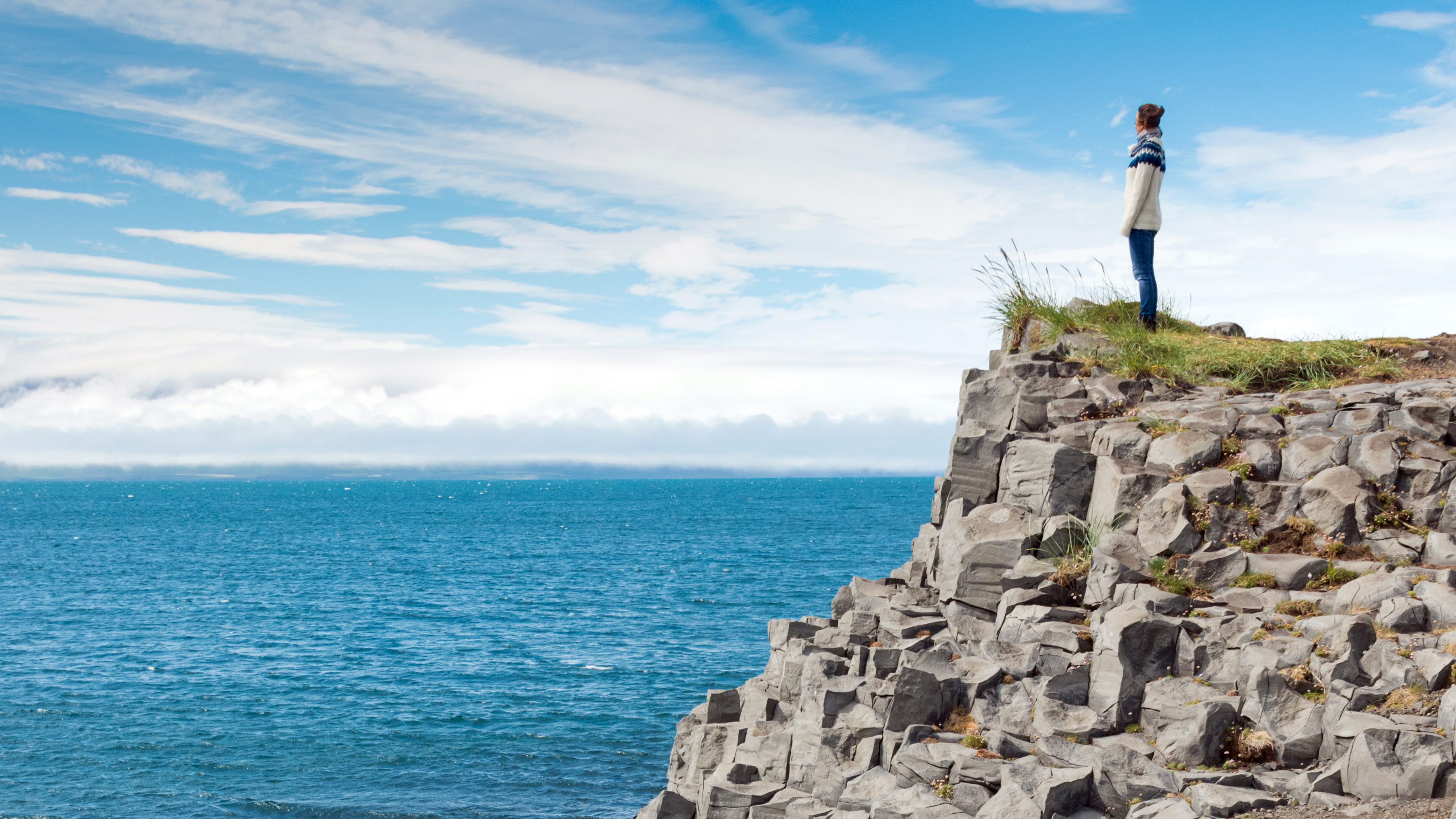 Eine Wanderin blick auf den Ozean an der steinigen Küste von Island.