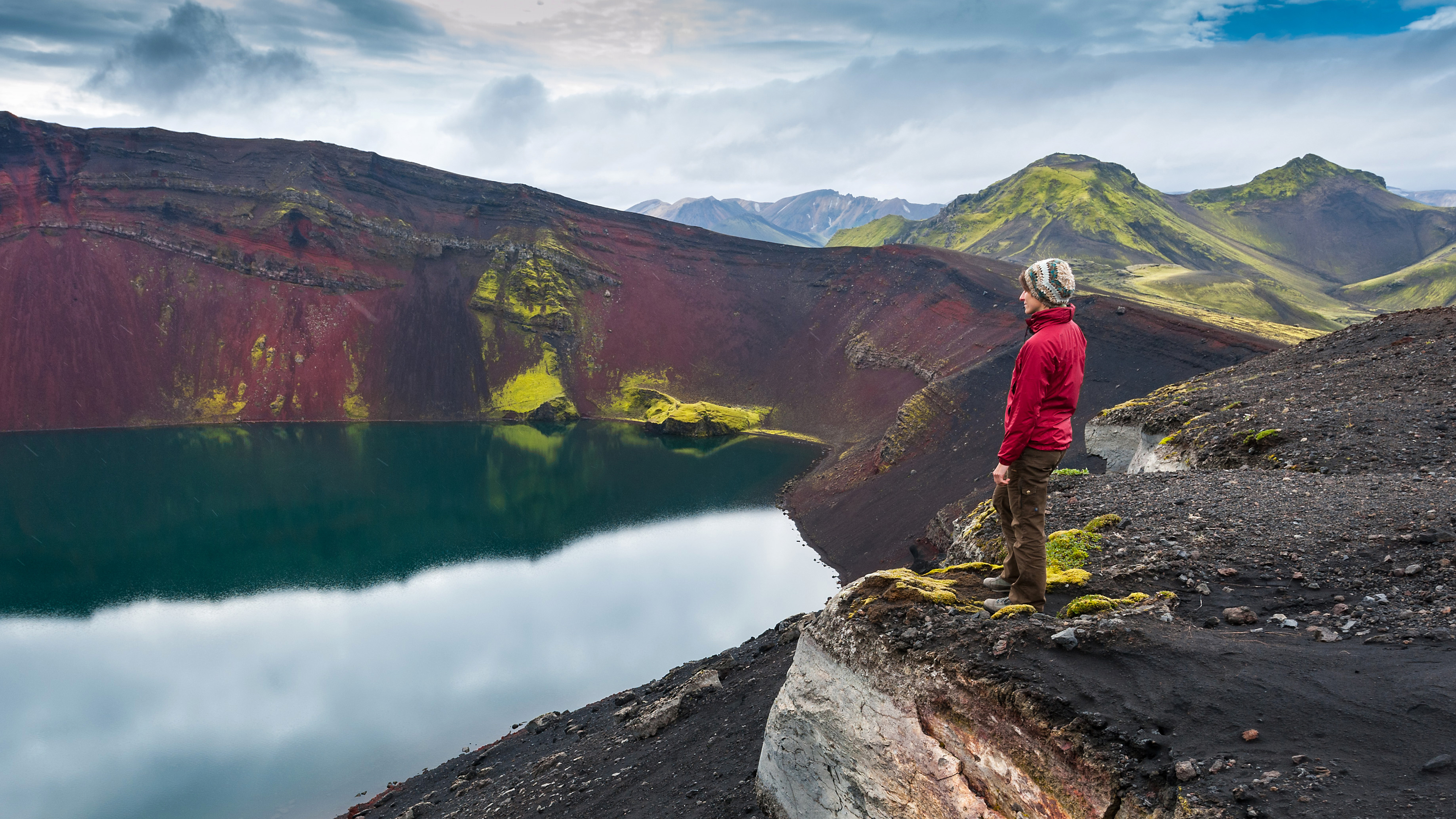 Vulkankrater Hochland Island, Frau schaut auf den Kratersee. Im Hintergrund viele Berge aus Geröll und grünen Islandmoos.