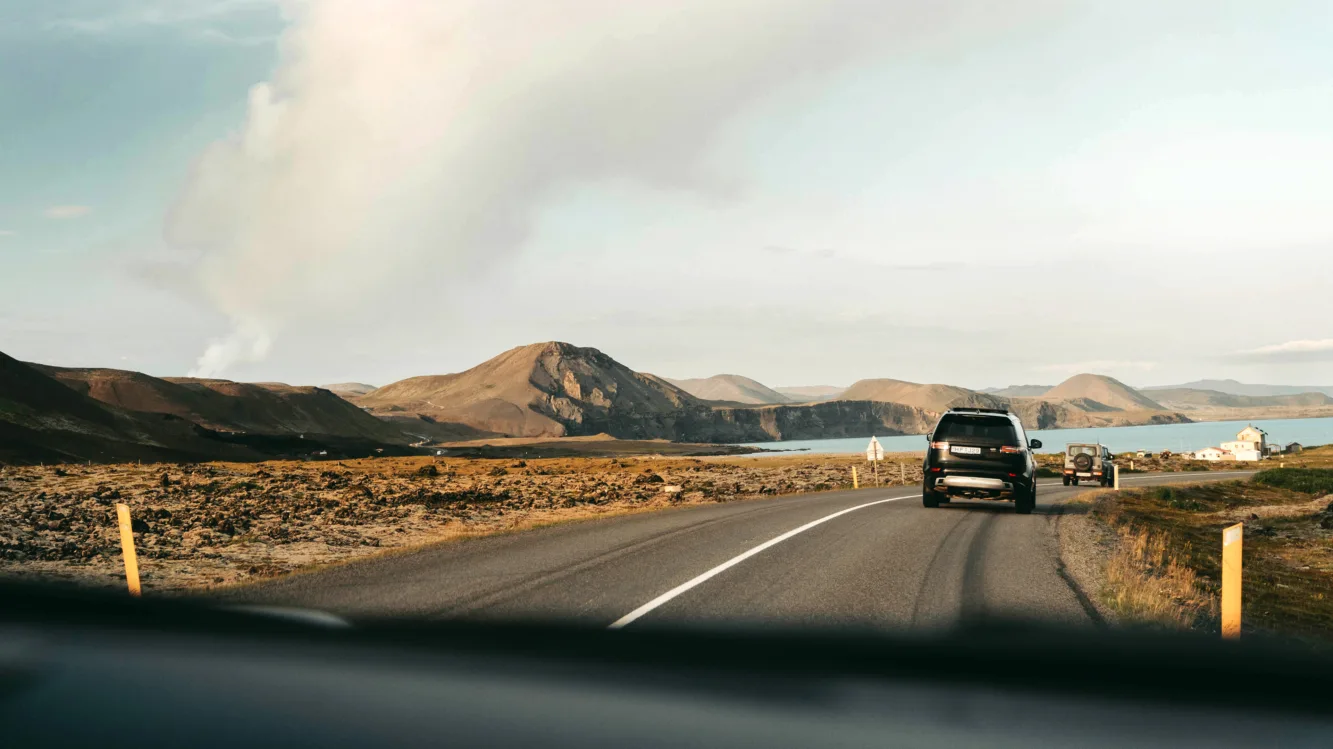 Aufnahme aus einer Autofrontscheibe mit Blick auf die Straße mit mehreren Autos und Meer und Bergen im Hintergrund
