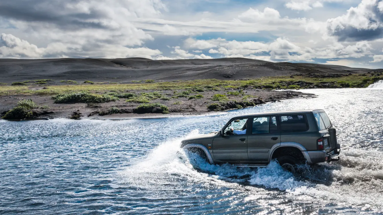 Flussdurchquerung Jeep Island Ein grauer Jeep fährt geradewegs durch einen Fluss im isländischen Hochland, um auf die andere Seite zu gelangen