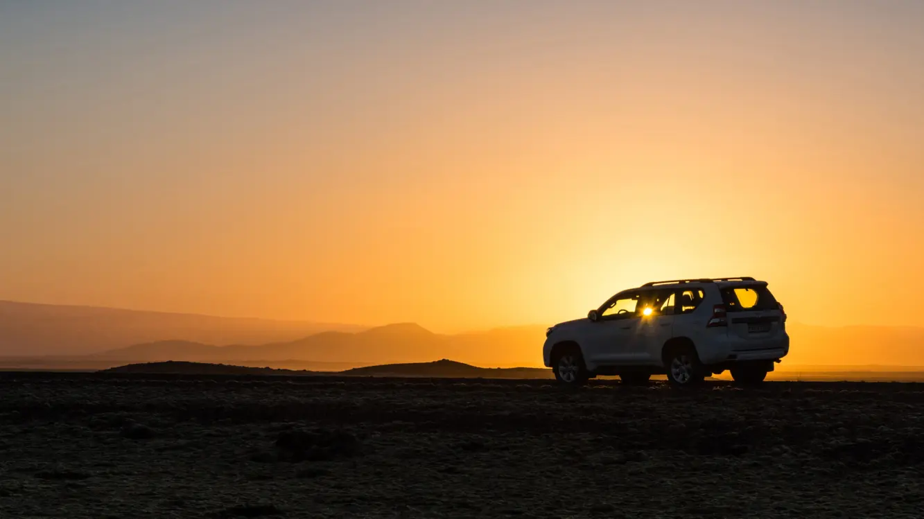 Jeep Sonnenuntergang Island Ein Jeep, der beim wunderschönen gelb-orangenen Sonnenuntergang in isländischer Landschaft steht