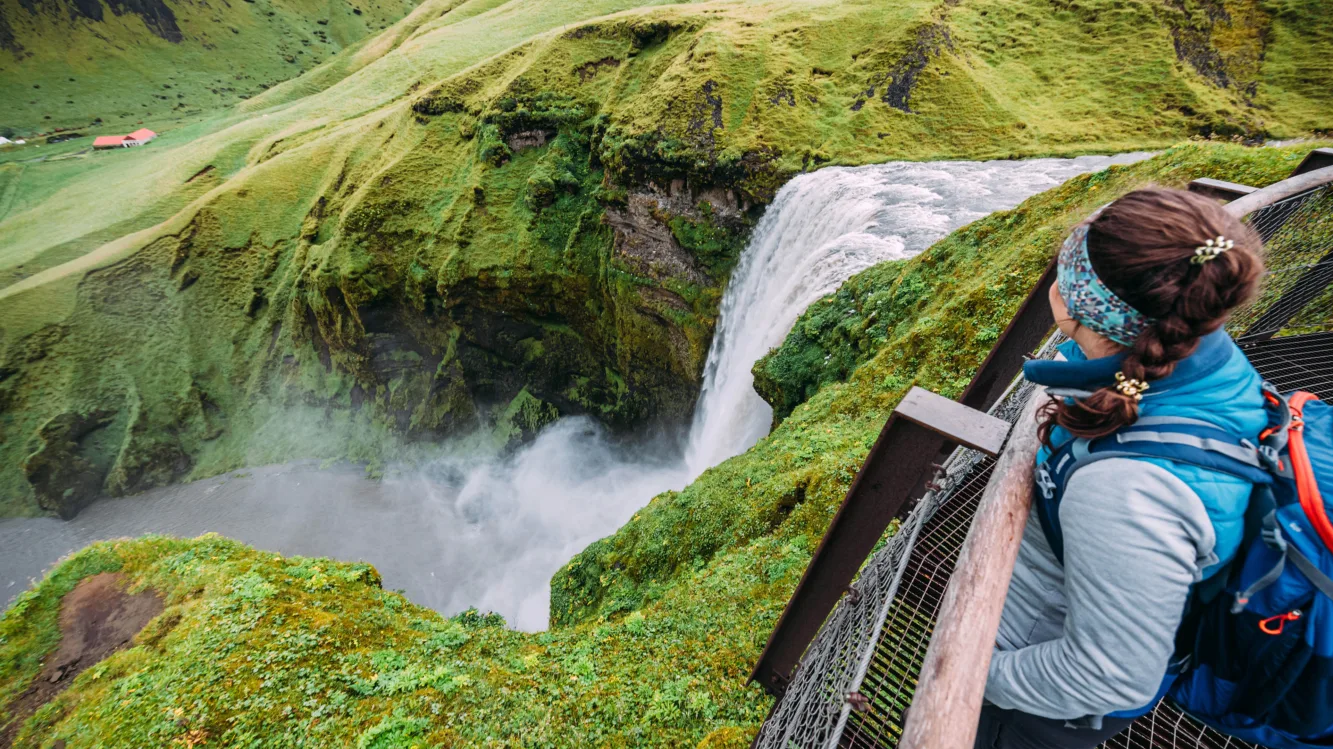 Frau steht am Wasserfall Skogafoss in Island, von oben fotografiert