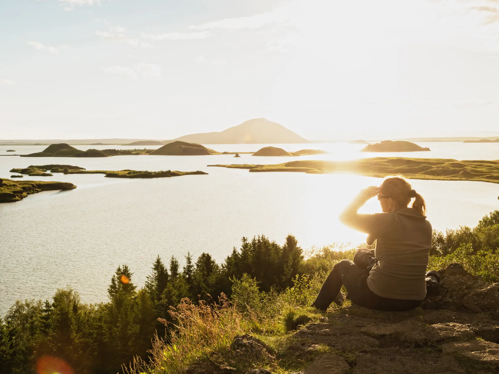 Frau sitzt bei Sonnenuntergang am See Myvatn in Island und genießt die schöne Aussicht