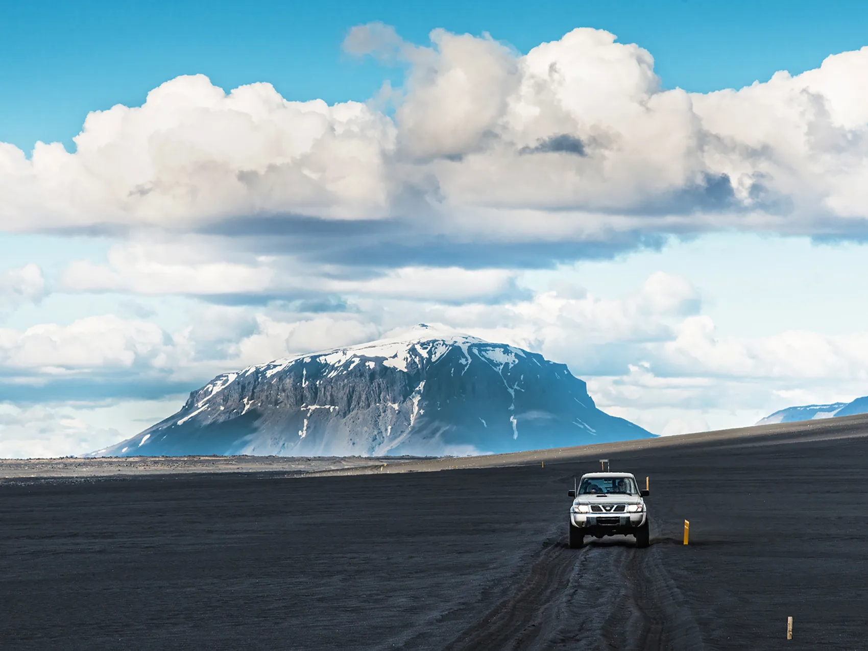 Jeep fährt in weiter isländischer Landschaft auf die Kamera zu mit einem Berg im Hintergrund