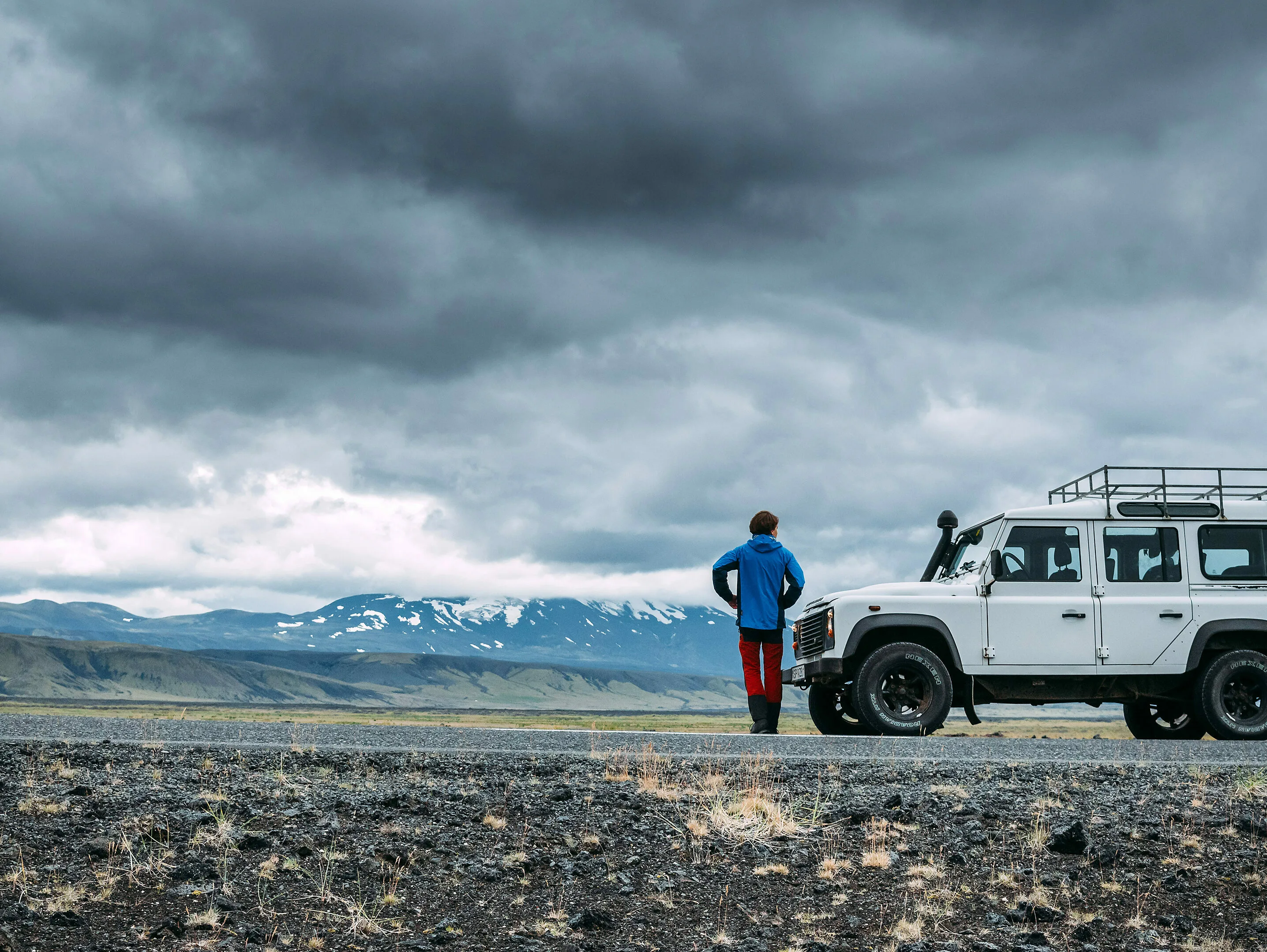 Ein Mann steht neben einem weißen Jeep in weiter und bewölkter isländischen Landschaft