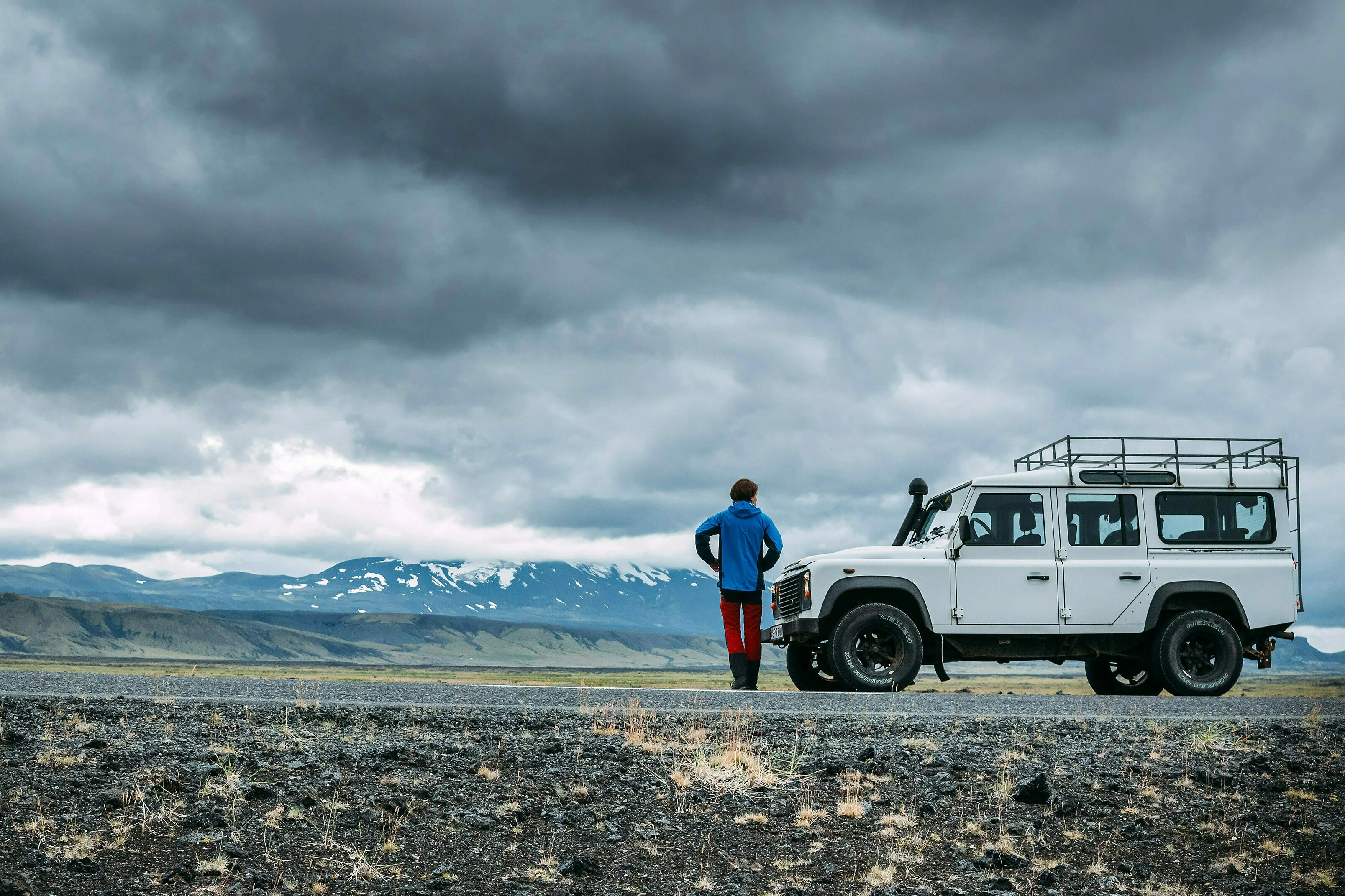 Ein Mann steht neben einem weißen Jeep in weiter und bewölkter isländischen Landschaft