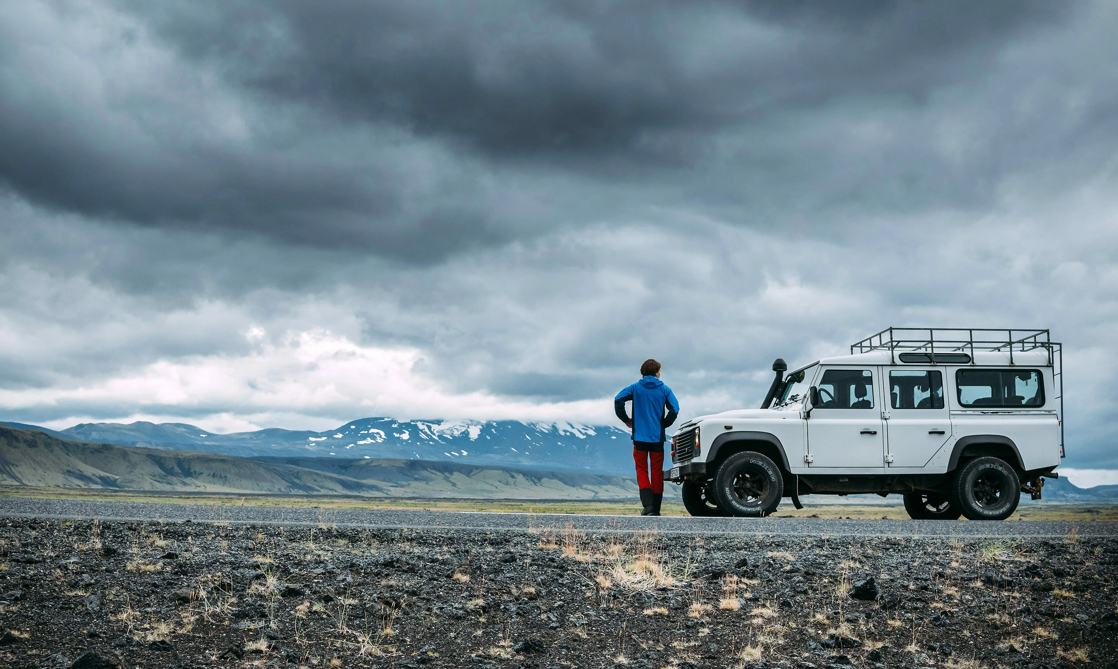 Ein Mann steht neben einem weißen Jeep in weiter und bewölkter isländischen Landschaft