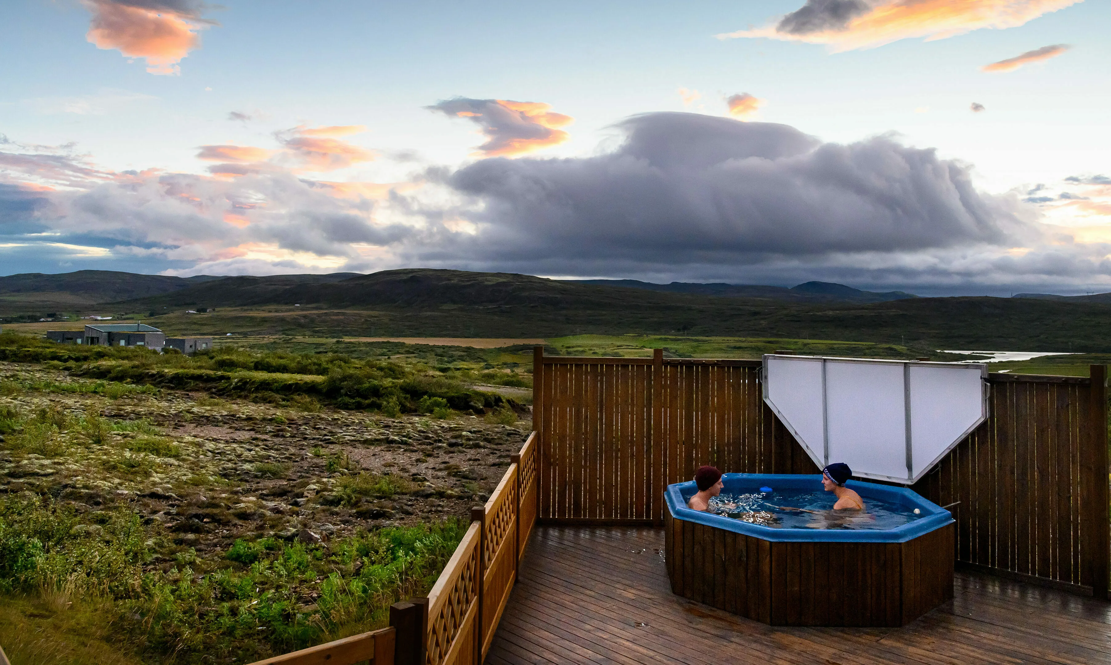 Pärchen im Hotpot Ferienhaus Island mit Wolken und isländischer Landschaft im Hintergrund