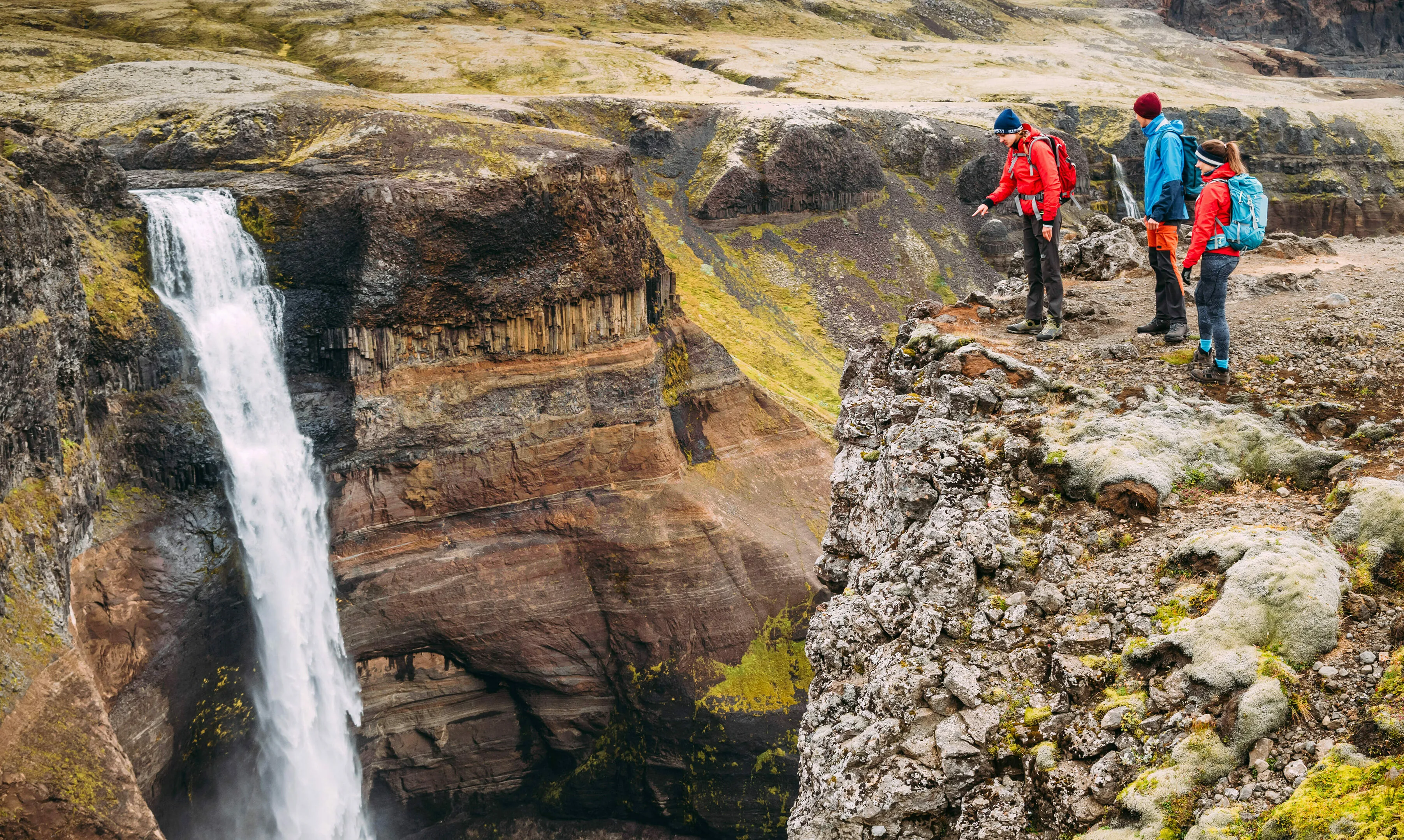 Eine kleine Wandergruppe genießt die Aussicht auf einen Wasserfall in Island