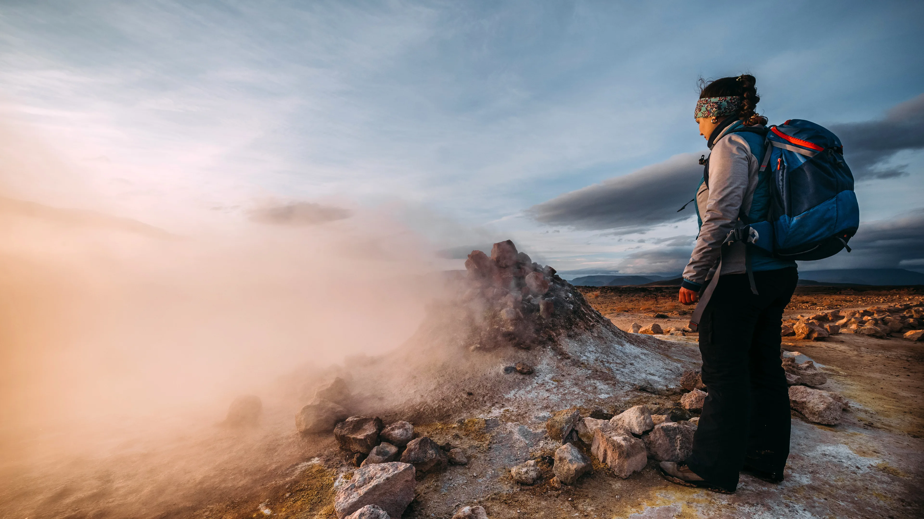 Frau am Dampffumarole Namafjall auf Island, Nebelschwaden, blauer Himmel mit Wolken, felsige Landschaft