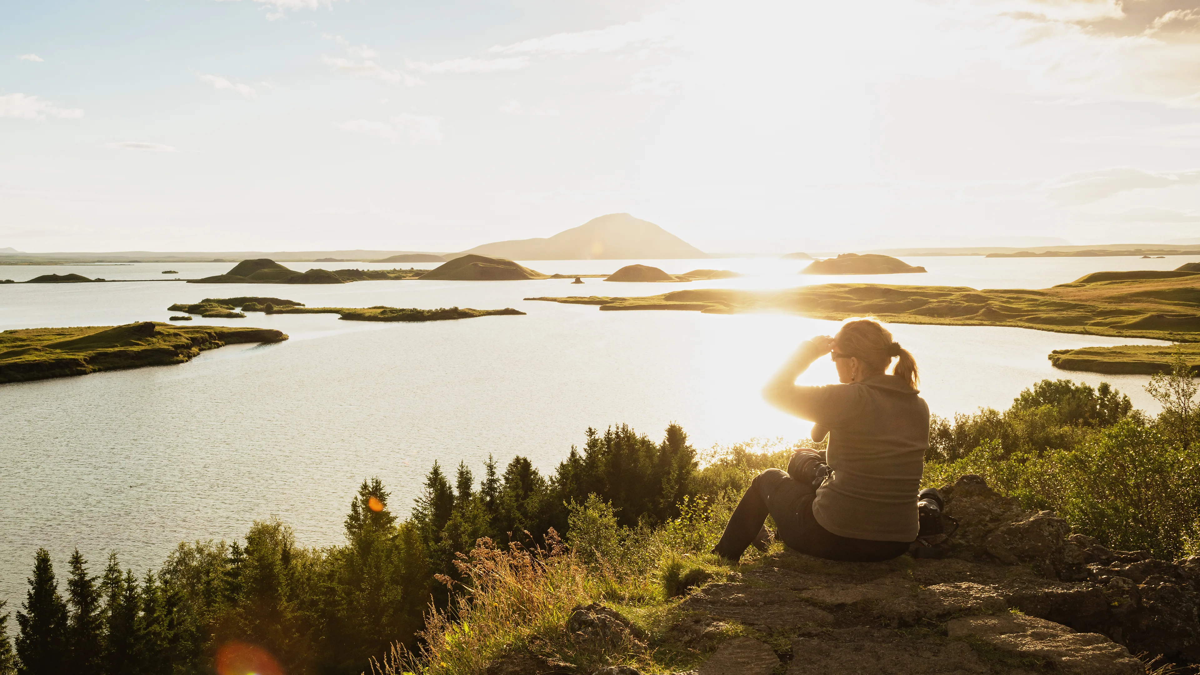 Frau sitzt bei Sonnenuntergang am See Myvatn in Island und genießt die schöne Aussicht