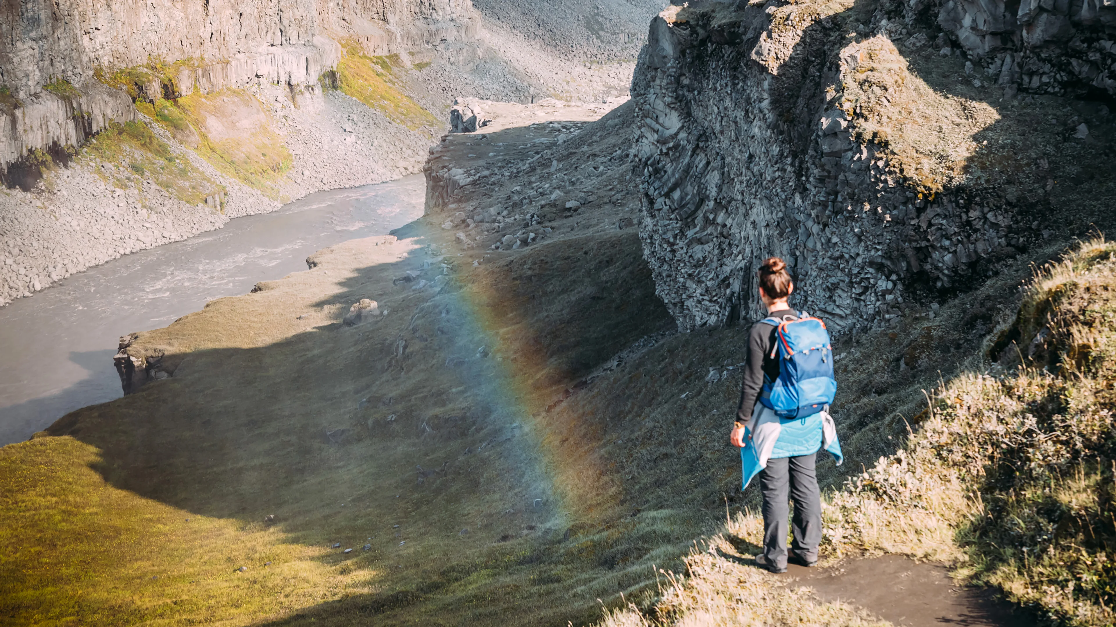 Frau steht über dem Jökulsargljufur Canyon in Island und schaut hinein, ein kleiner Regenbogen ist daneben zu sehen