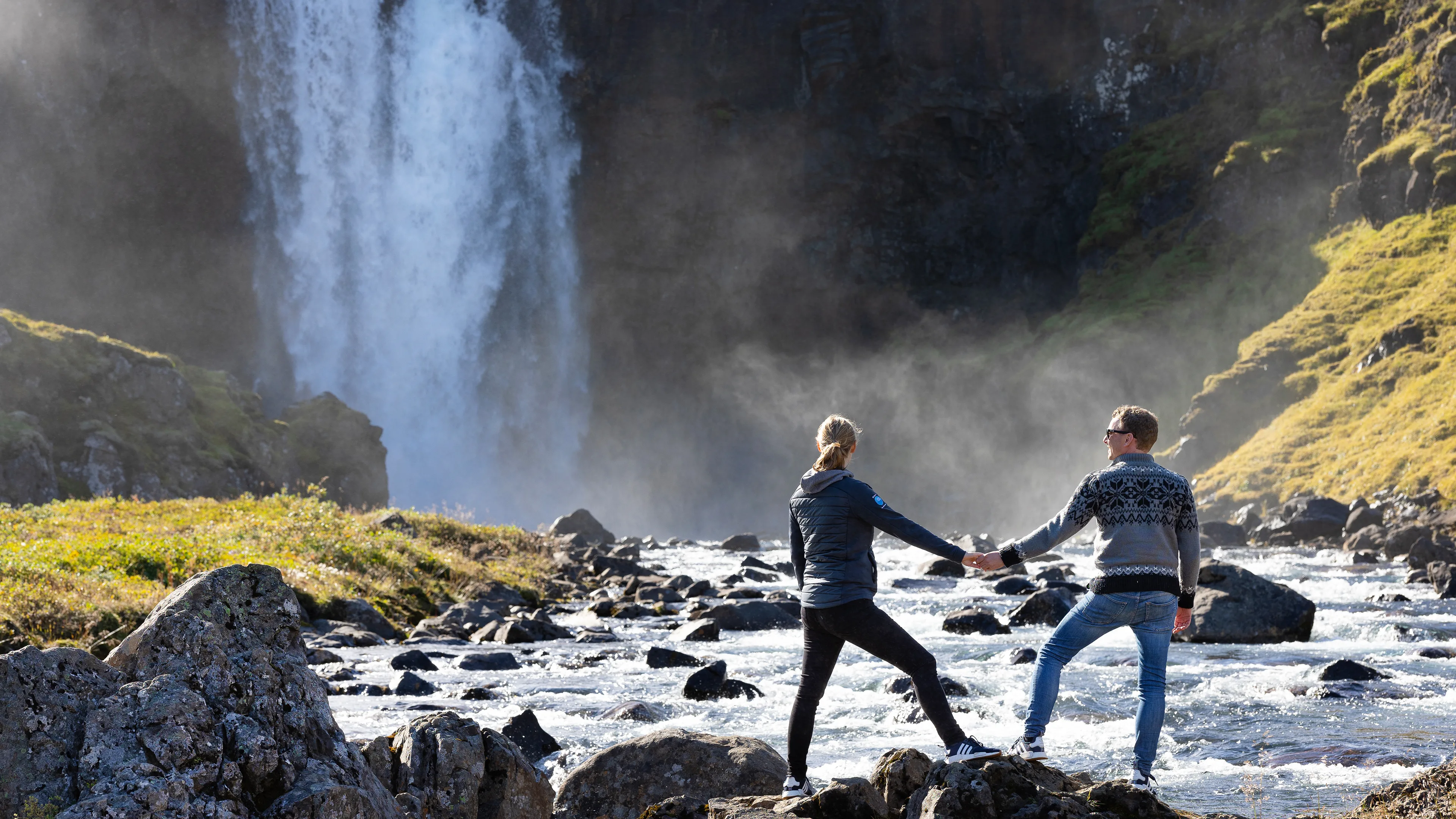 Paar steht händchenhaltend vor einem Wasserfall in Island