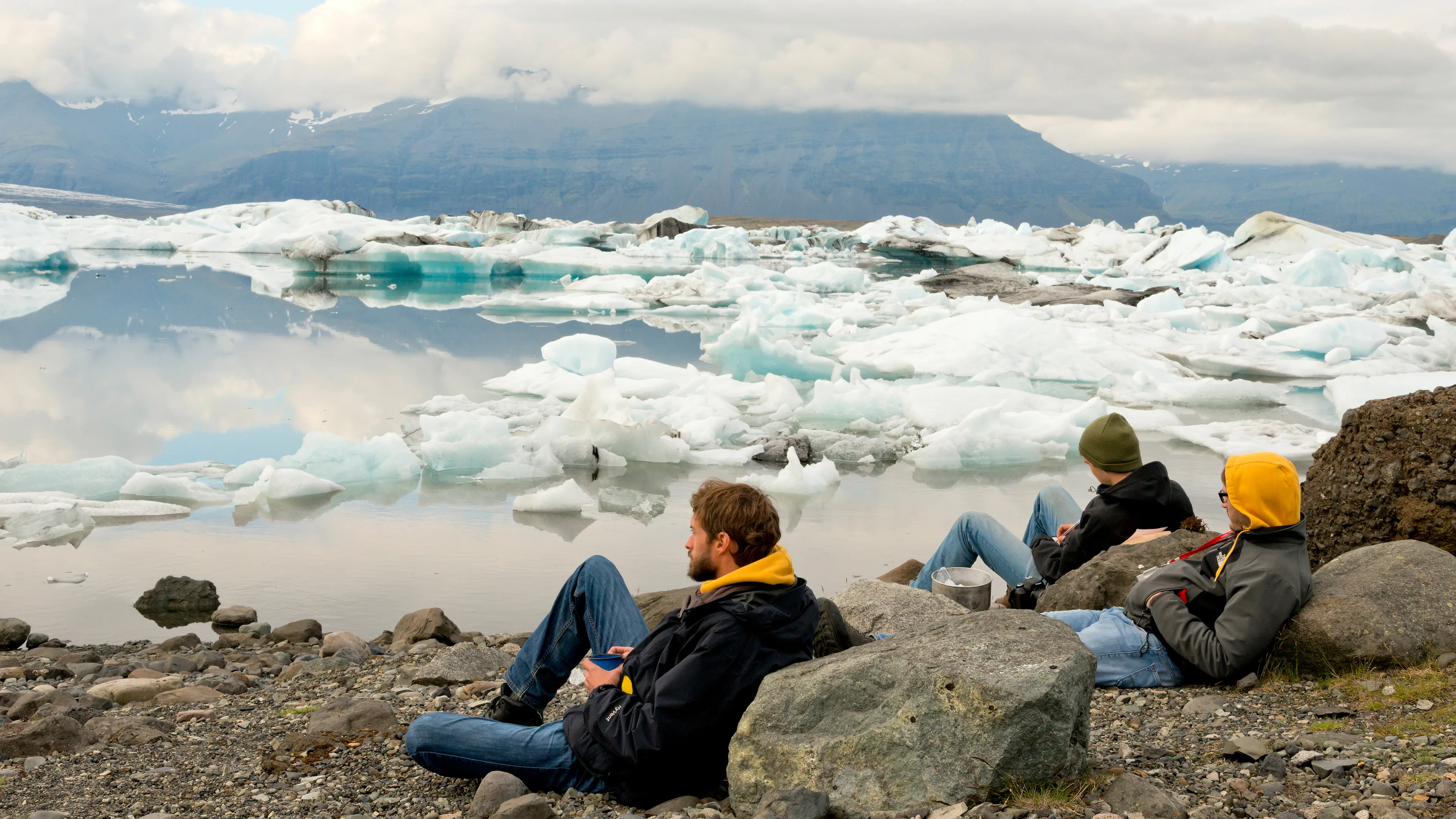 Reisende sitzen neben der Gletscherlagune Jökulsarlon in Island und genießen den Ausblick auf die Eisberge
