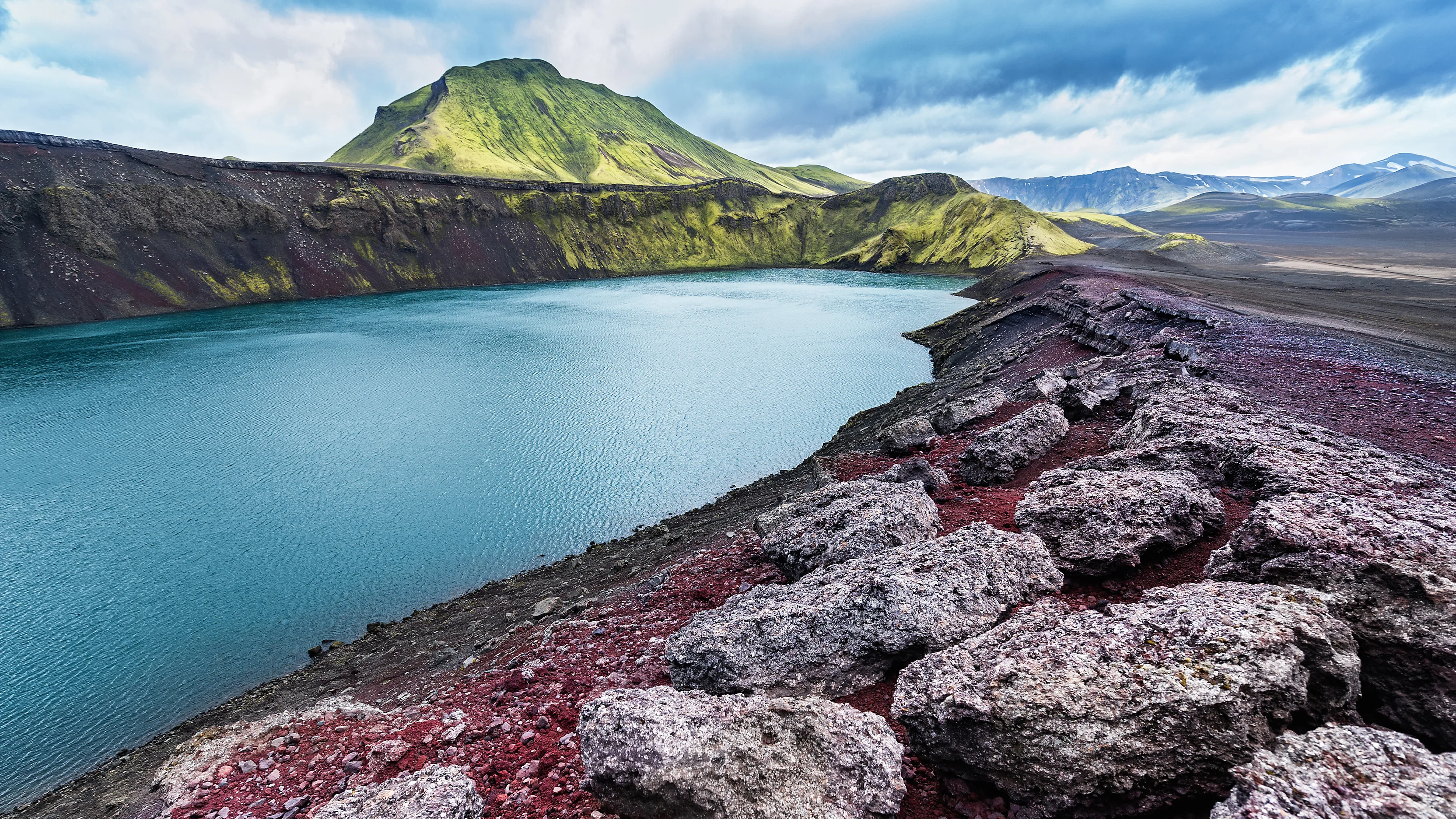 Schöner rötlicher Vulkankrater mit See in der Mitte und isländischer Landschaft umherum