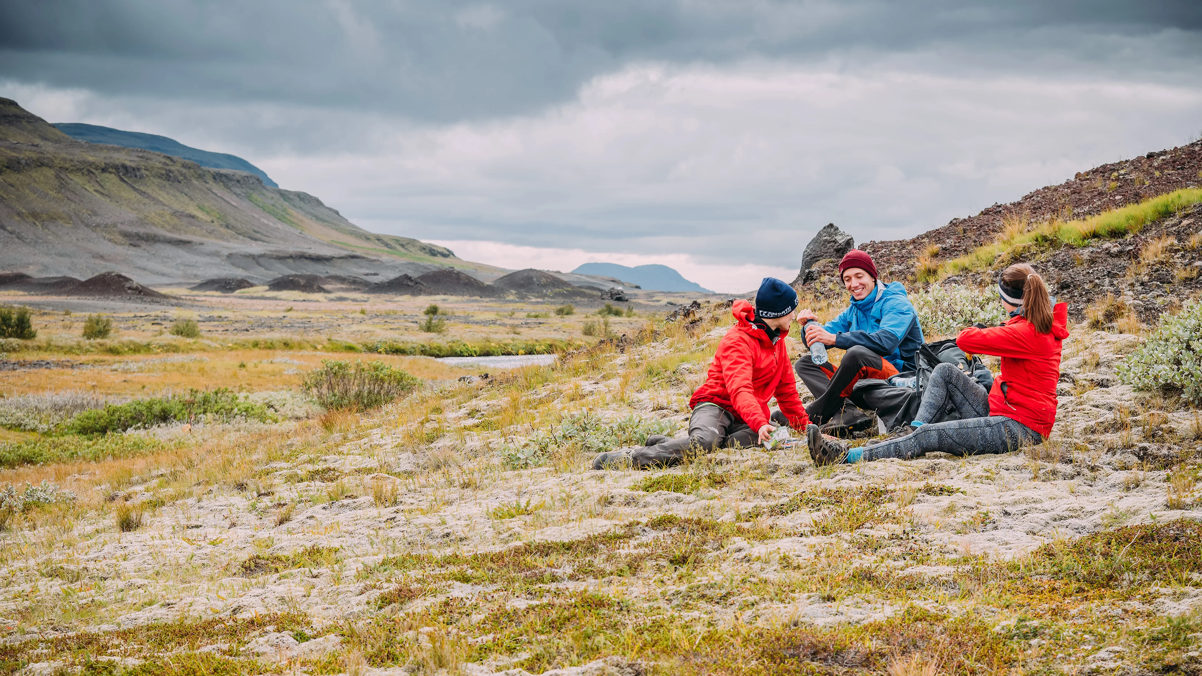 Drei Personen sitzen auf einer Wiese und machen Pause von ihrer Wanderung in der schönen isländischen Landschaft