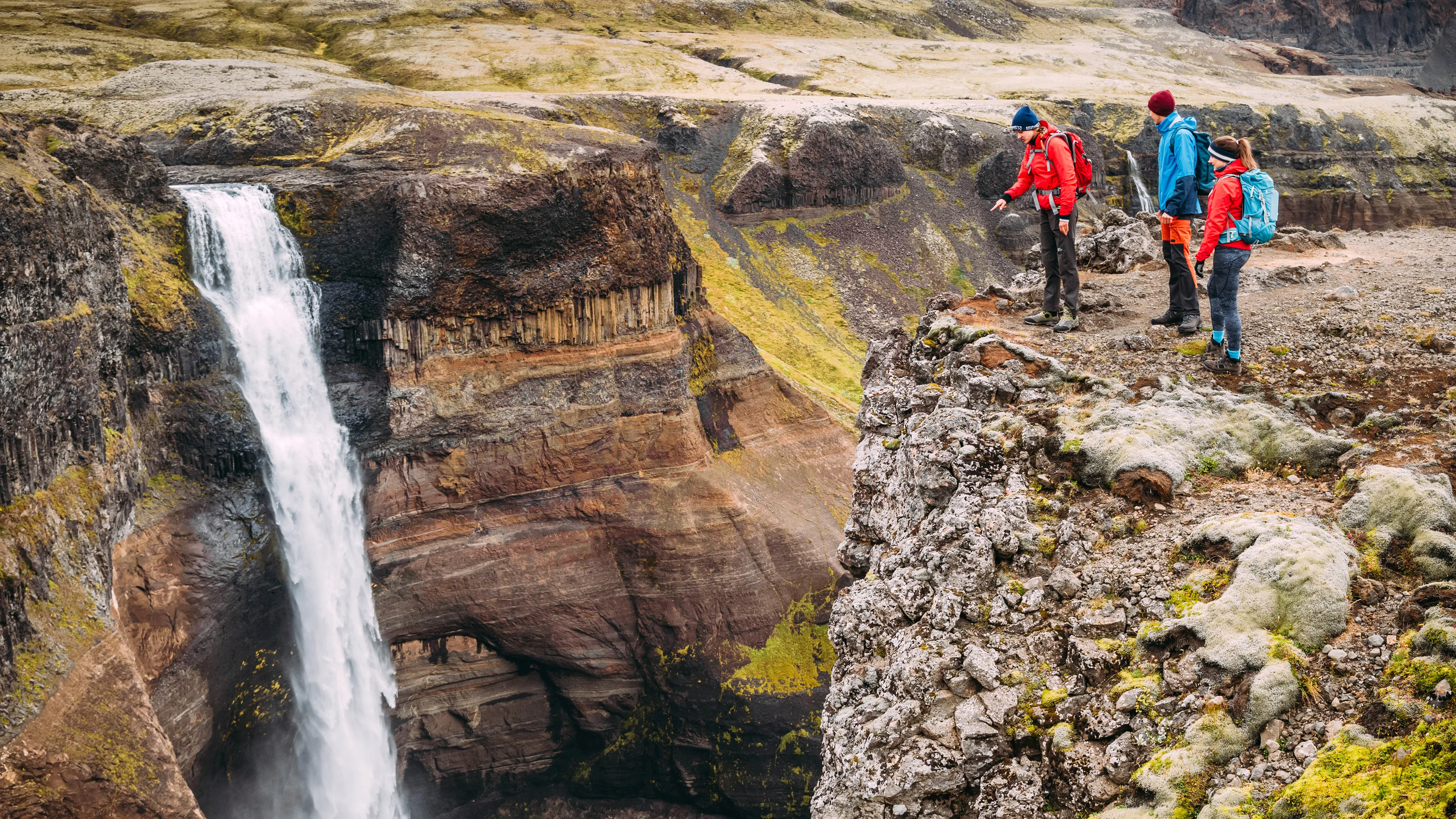 Eine kleine Wandergruppe genießt die Aussicht auf einen Wasserfall in Island