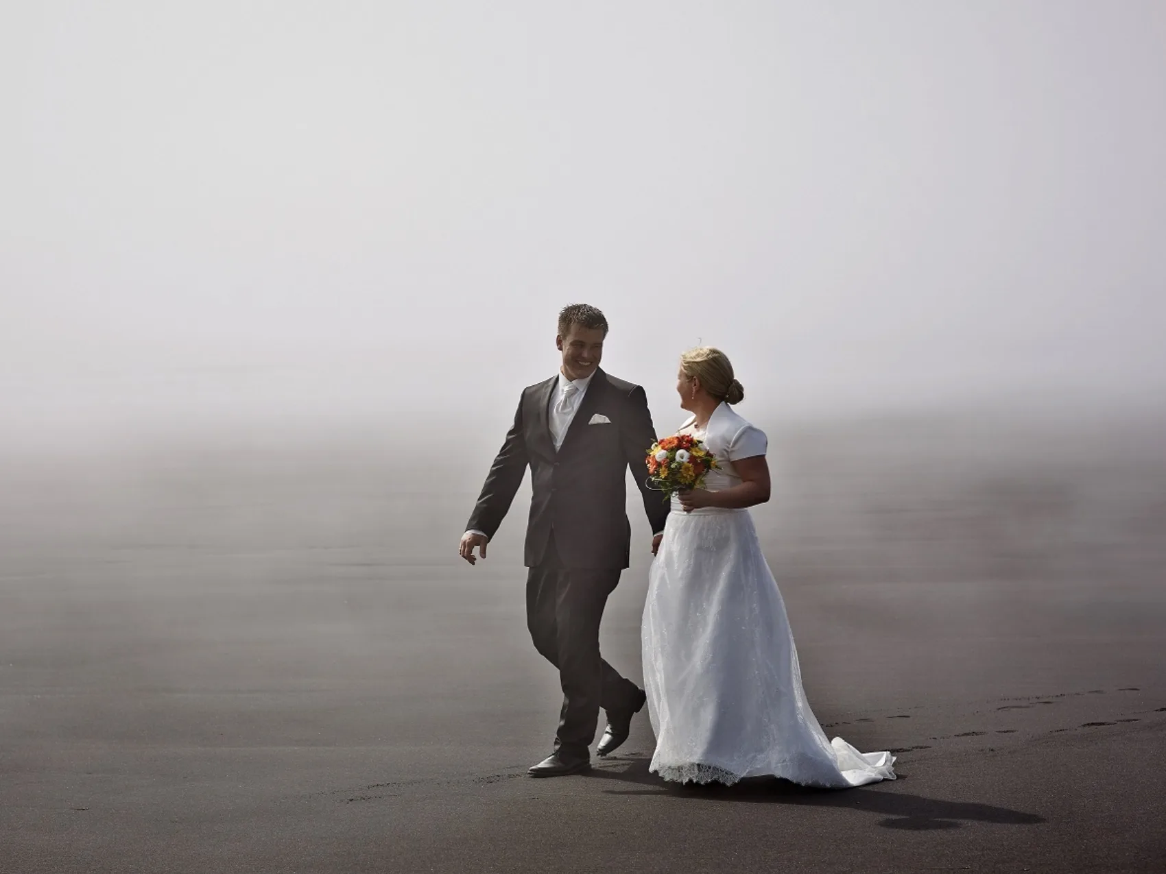 Lachendes Hochzeitspaar läuft im Nebel einen Strand entlang