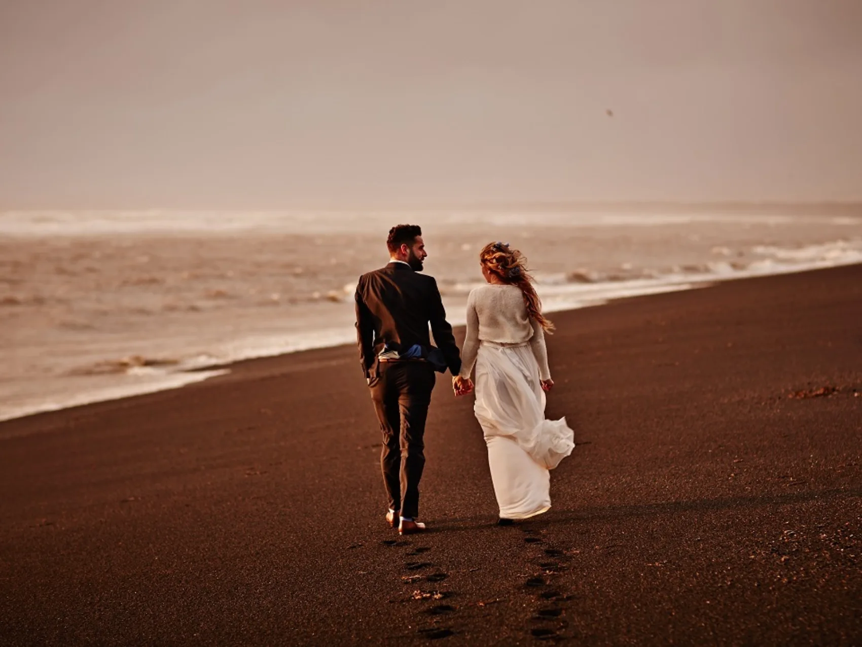 Hochzeitspaar läuft bei windigem Wetter einen schönen Strand entlang