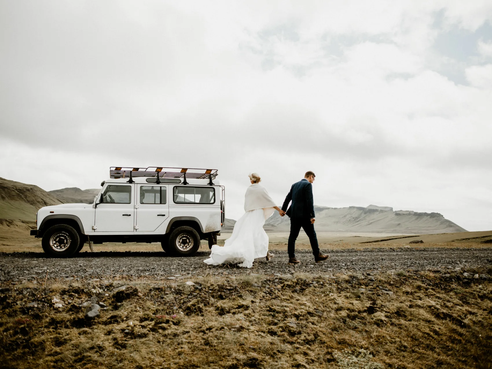 Pärchen vor einem Jeep in schöner isländischer Landschaft mit Bergen im Hintergrund