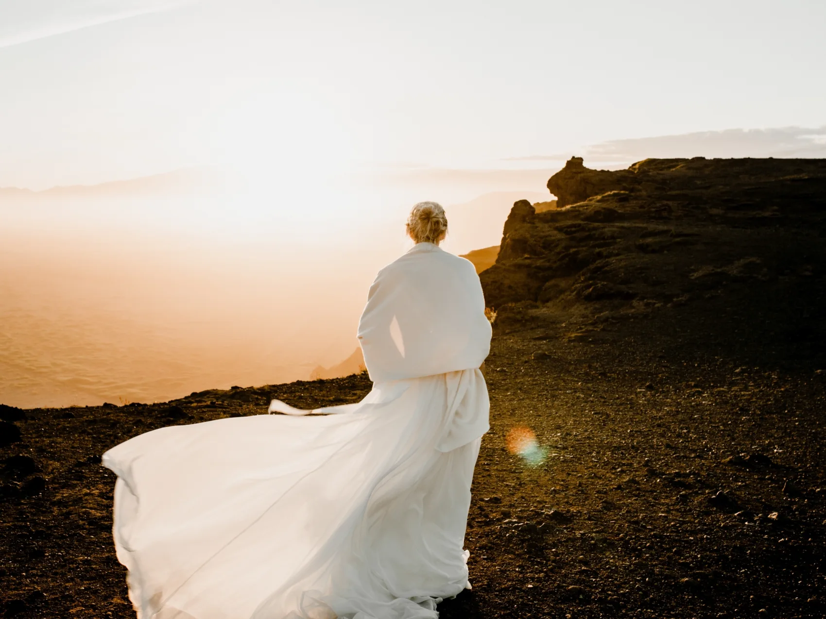 Heiraten in Island mit Katla Travel, Braut mit wehendem Kleid steht bei Sonnenuntergang auf einem Berg