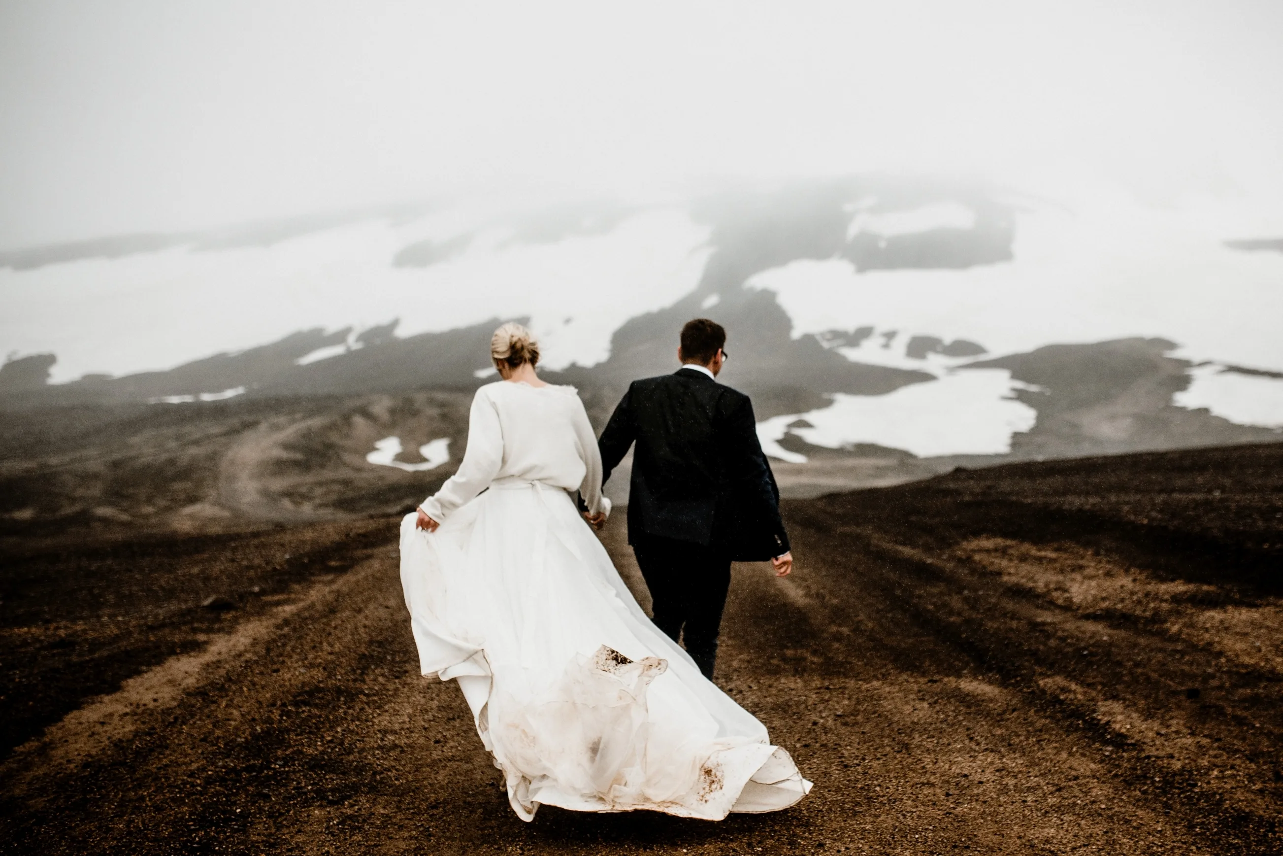 Hochzeitspaar läuft durch schöne isländische Landschaft, mit verschneiten Bergen im Hintergrund