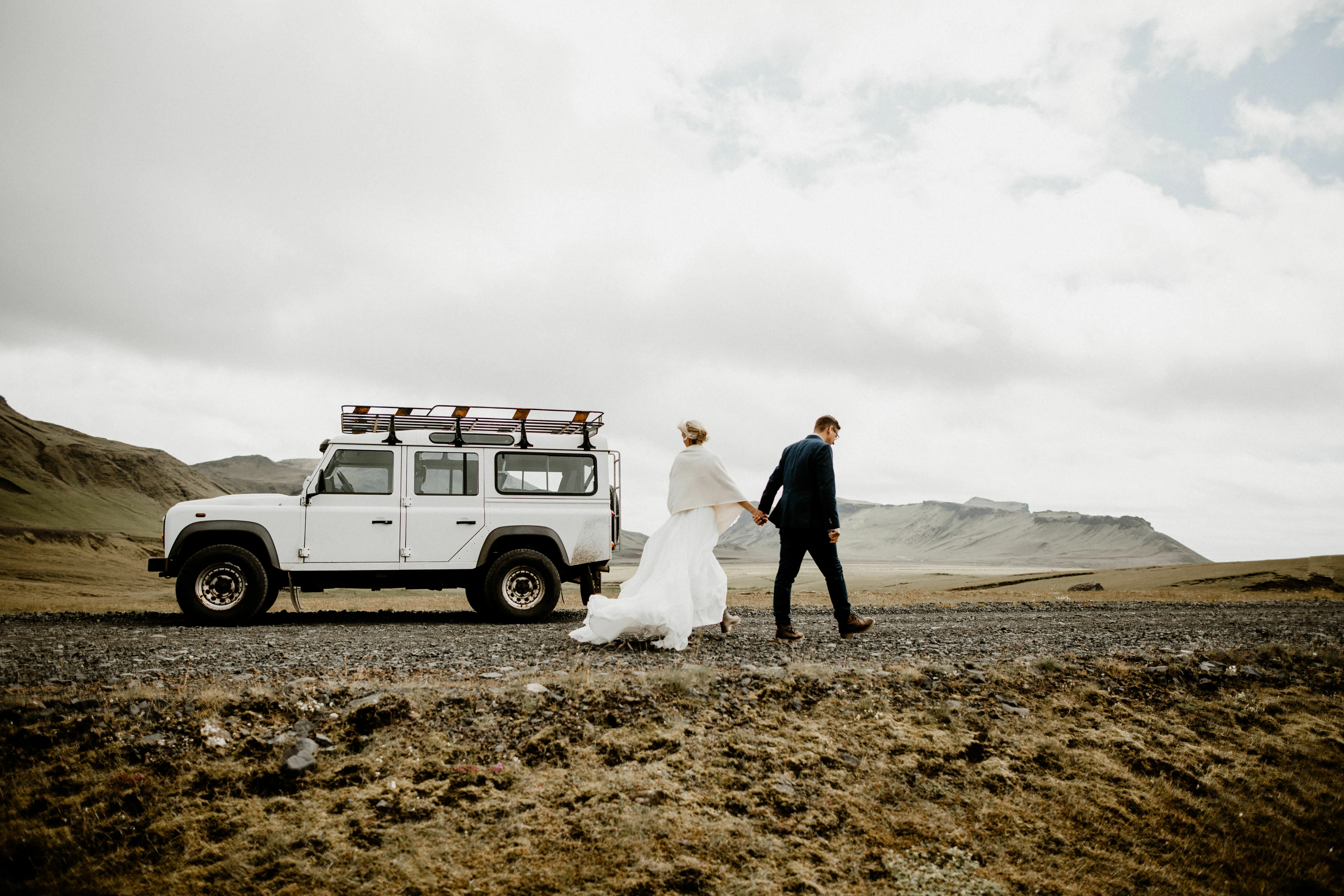 Pärchen vor einem Jeep in schöner isländischer Landschaft mit Bergen im Hintergrund